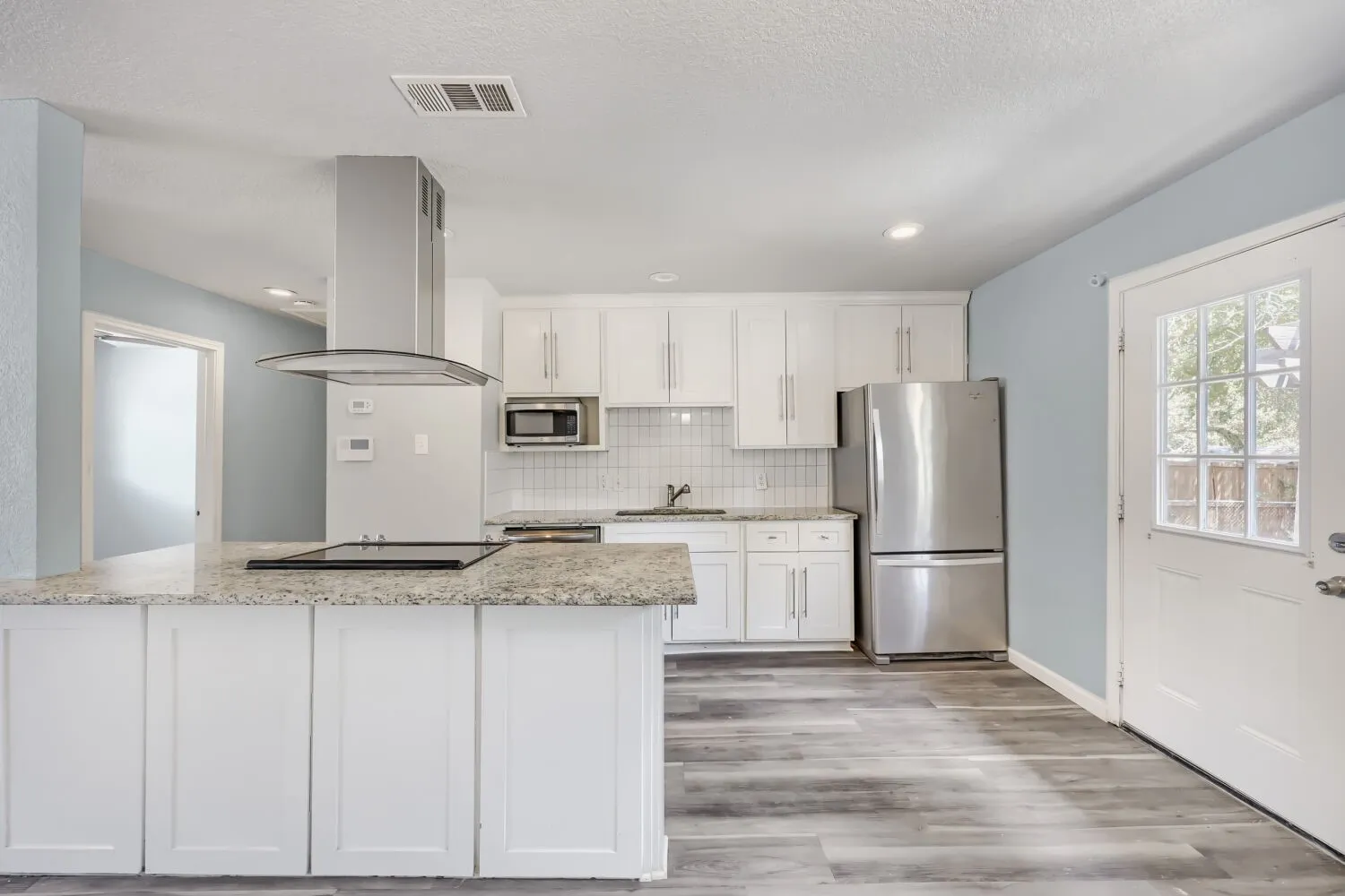 Kitchen featuring white cabinetry, stainless steel appliances, a kitchen island with cooktop, wood-finish flooring, and a white tile backsplash