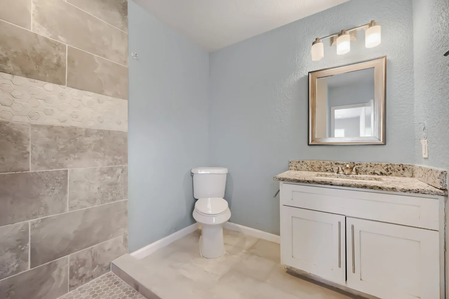 Shower with large format wall tiles and hexagonal accent, white vanity with stone countertop, and contemporary light fixture