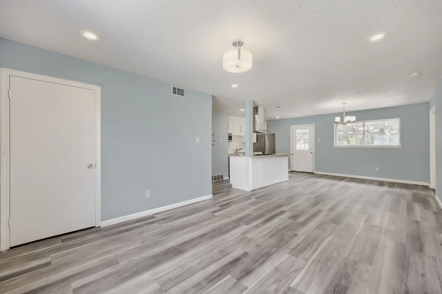 Recessed lighting, wood-finish flooring, white paneled cabinetry, stainless steel range hood, and a built-in kitchen island with a light-toned countertop