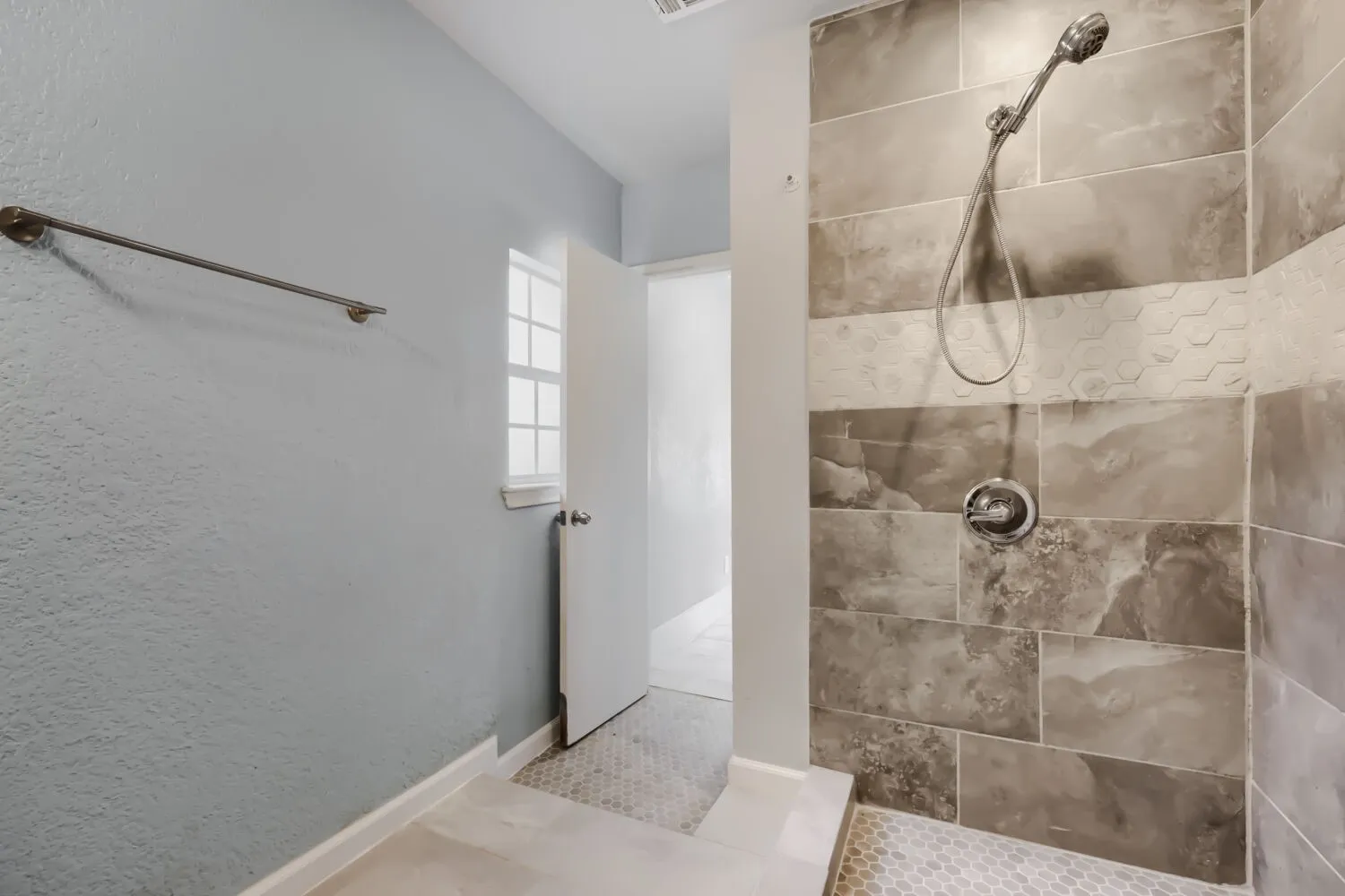 Modern spa-inspired ensuite featuring large-format tile walls in warm neutral tones, dual showerheads with chrome fixtures, a spacious walk-in shower with glass enclosure, and neutral tile flooring throughout
