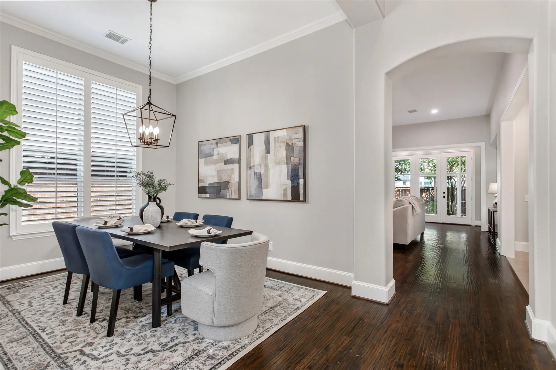 Dining room with crown molding, plantation shutters on oversized windows, and a new 2026 lantern
chandelier. An arched opening and hardwood hallway lead to the family room.