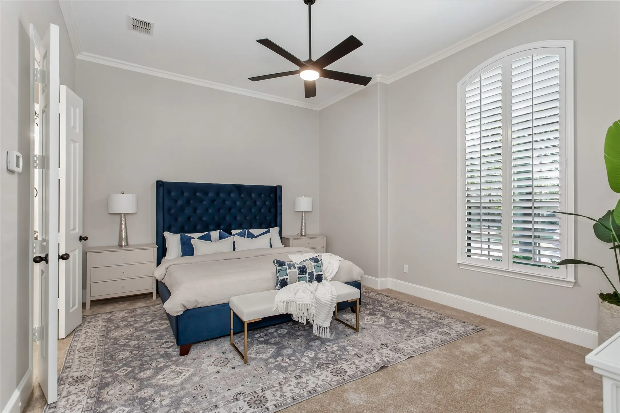 Downstairs primary bedroom with crown molding, an arched window with plantation shutters, and new
2026 carpet. New ceiling fan with an LED light.