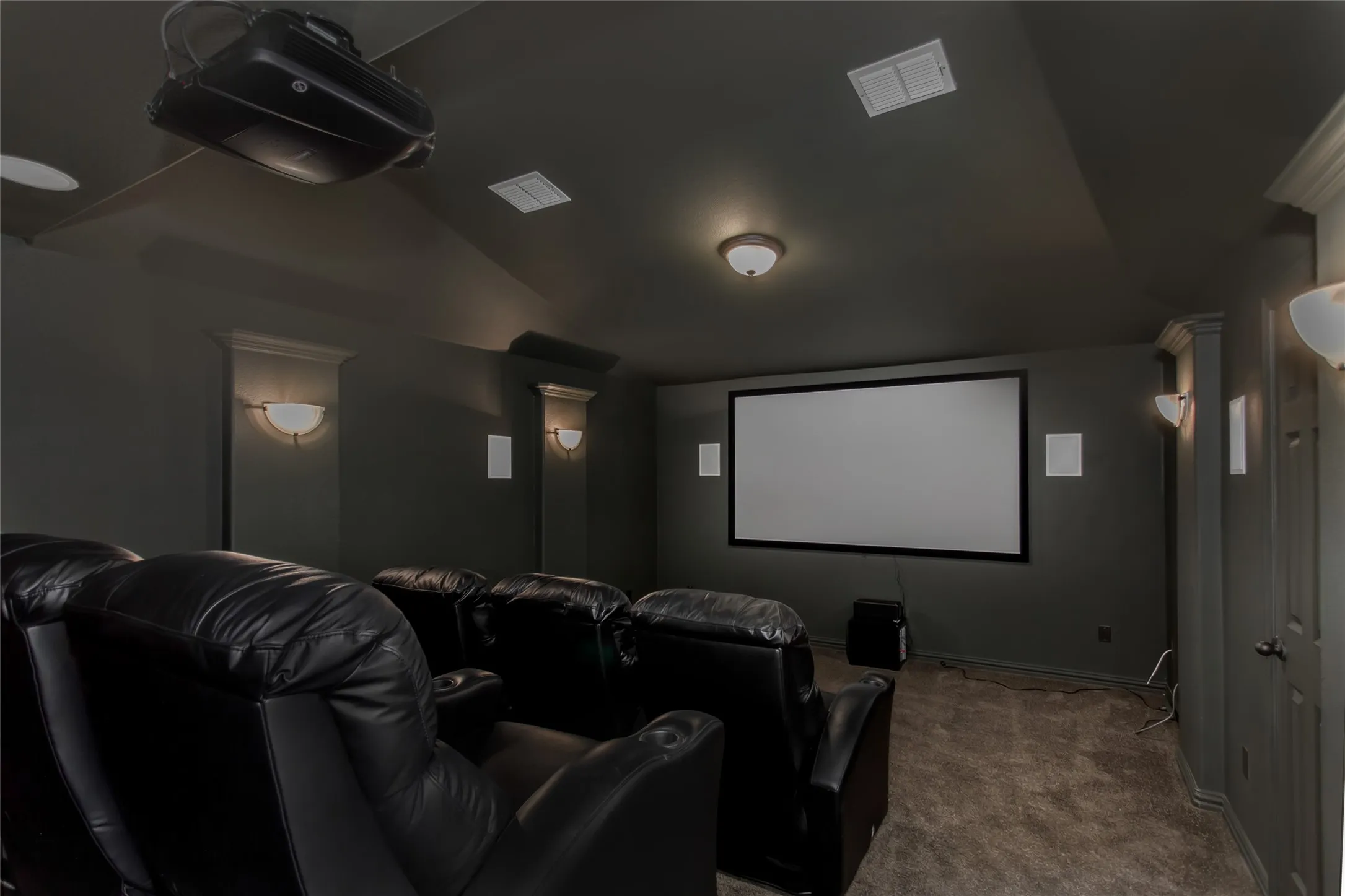 Dedicated media room with a projection screen, ceiling-mounted projector, in-wall speakers, and wall
sconces. Dark walls and carpet for a theater setting.
