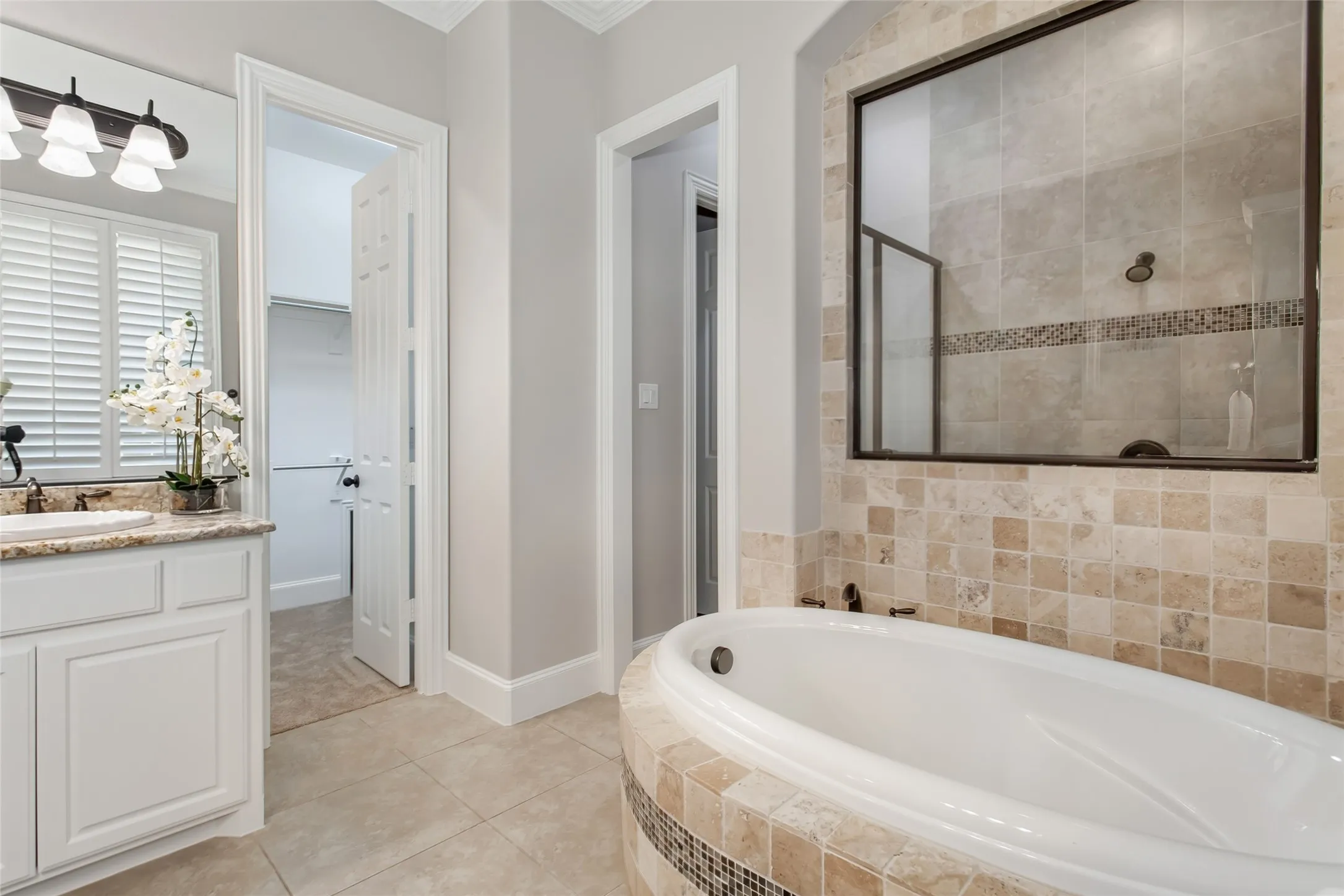 Walk-in shower with travertine tile, a glass mosaic accent band, and oil-rubbed bronze fixtures beside
the garden tub. Doorway to the walk-in closet on the left.
