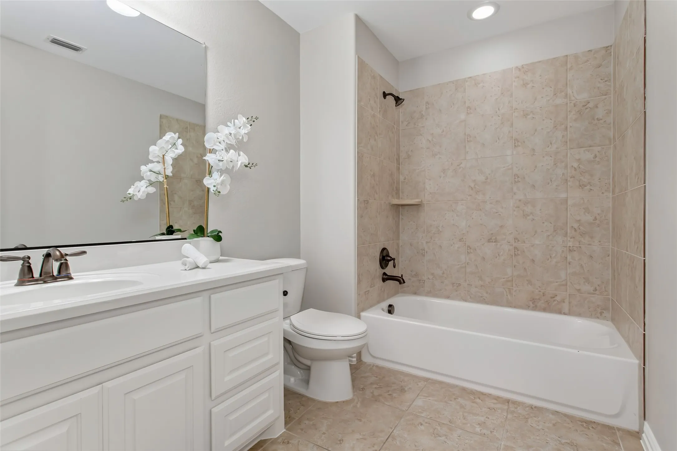 Full bath with a tub and shower combination in a tile surround, a single vanity with white cabinetry, and
tile flooring. Oil-rubbed bronze fixtures.