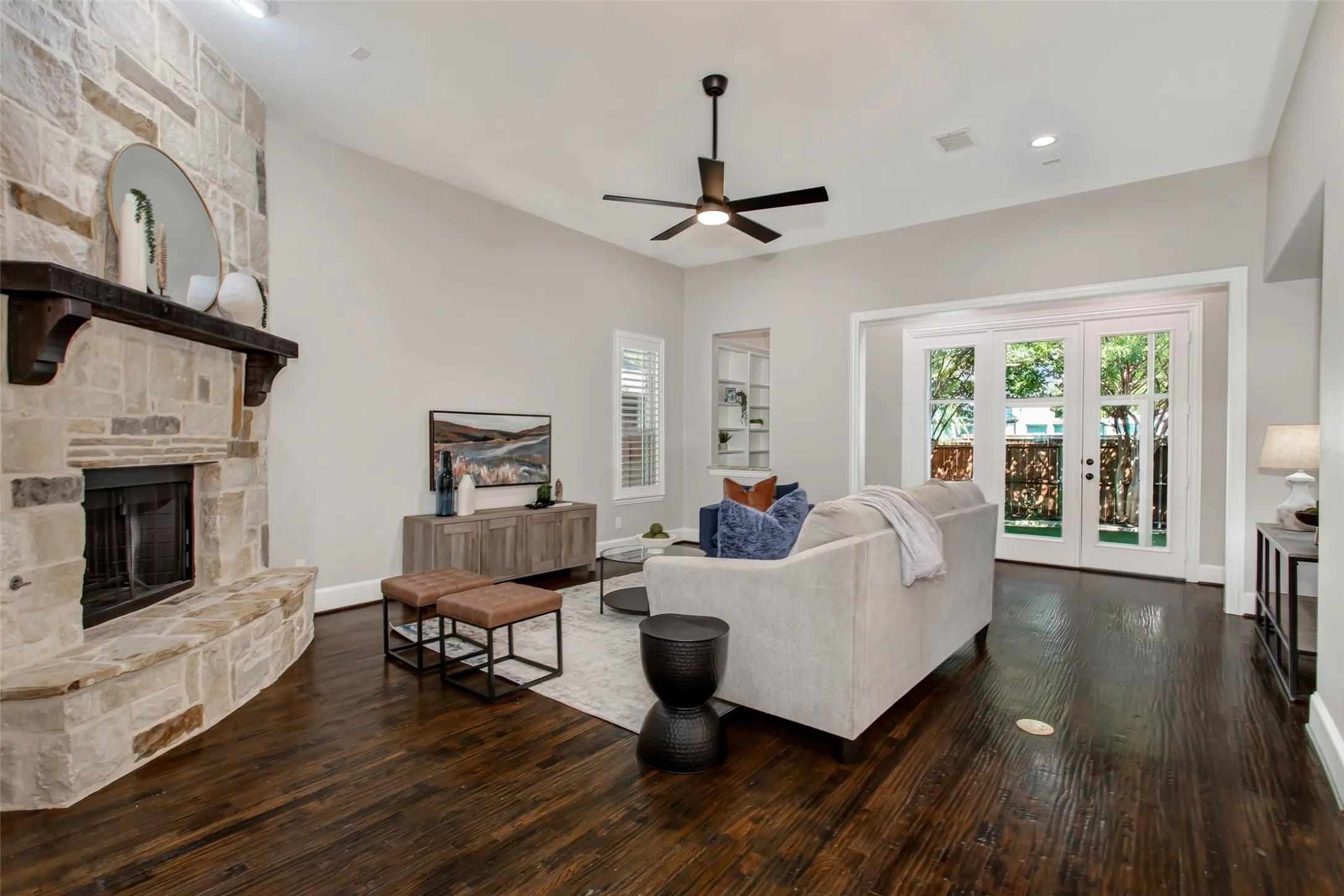 A gas-start stone corner fireplace with a raised hearth and dark wood beam mantel anchors the room. A
wall of French doors opens to the enclosed sunroom and turf backyard.