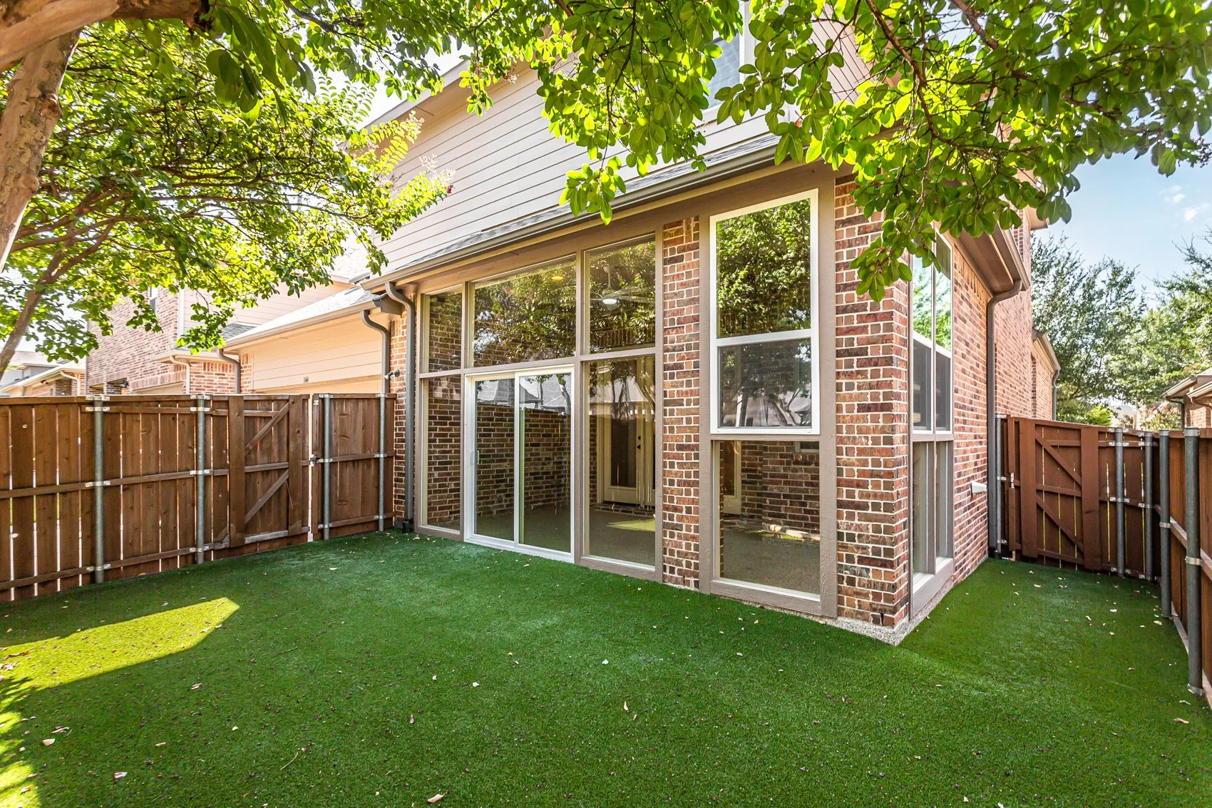 Rear elevation of brick and siding with the glass-enclosed sunroom opening to the turf yard through a
sliding door. Gated side yard access on both sides.