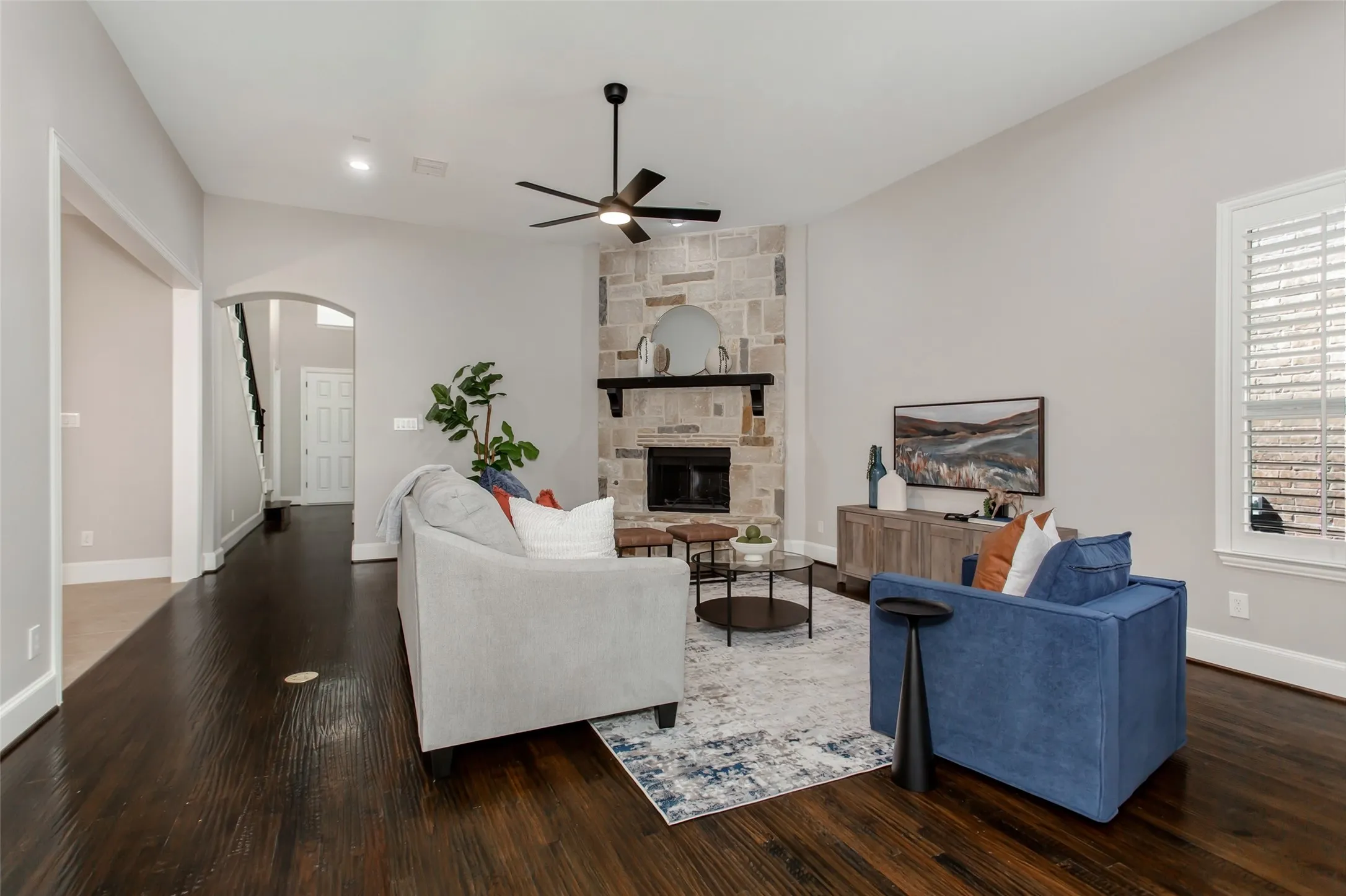 View toward the stone fireplace, with an arched opening to the foyer and staircase. Recessed lighting
and a new 2026 ceiling fan with an LED light overhead.