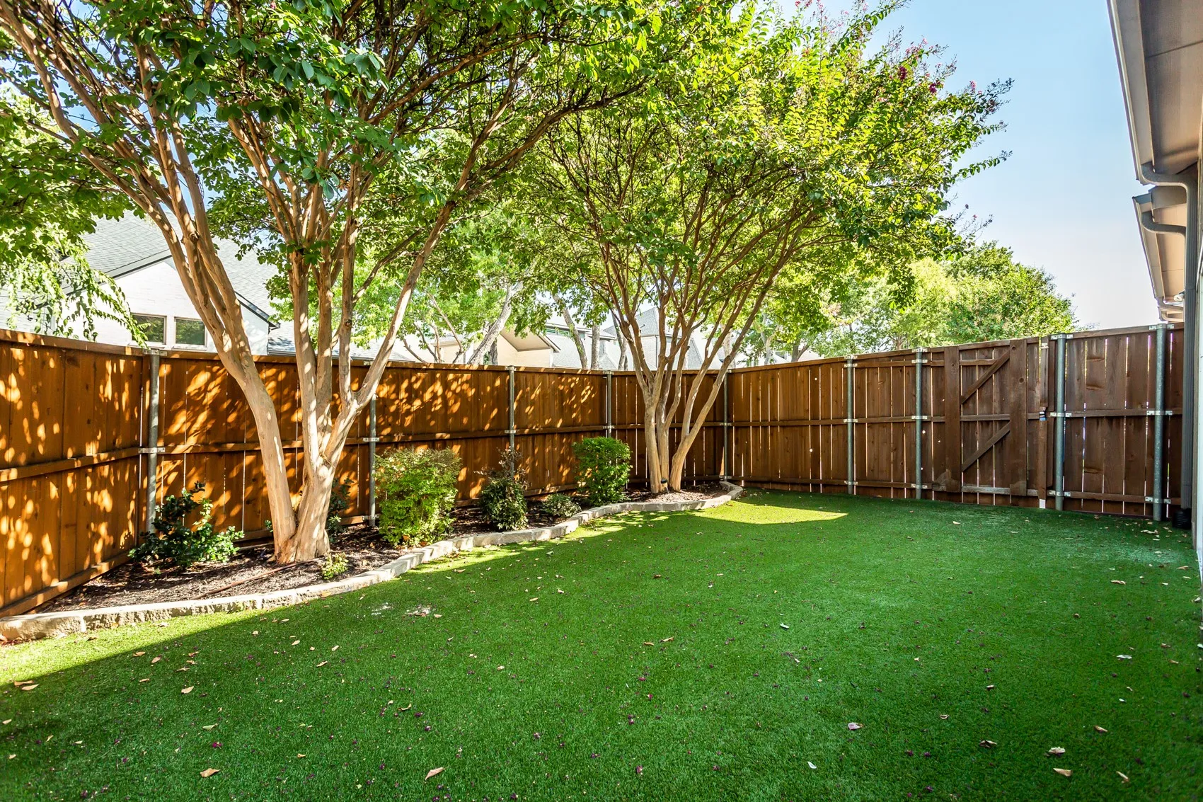 Turf yard shaded by mature crape myrtles with a stone-bordered landscape bed. Stained privacy fence
on steel posts with a gate to the side yard.
