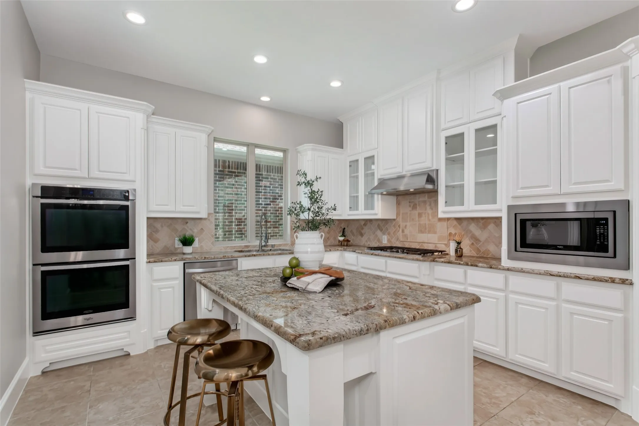 White cabinetry with glass-front uppers, granite countertops, and a tumbled stone herringbone
backsplash. Stainless double wall ovens, 5-burner gas cooktop with vent hood, built-in microwave,
dishwasher, and a center island with seating.