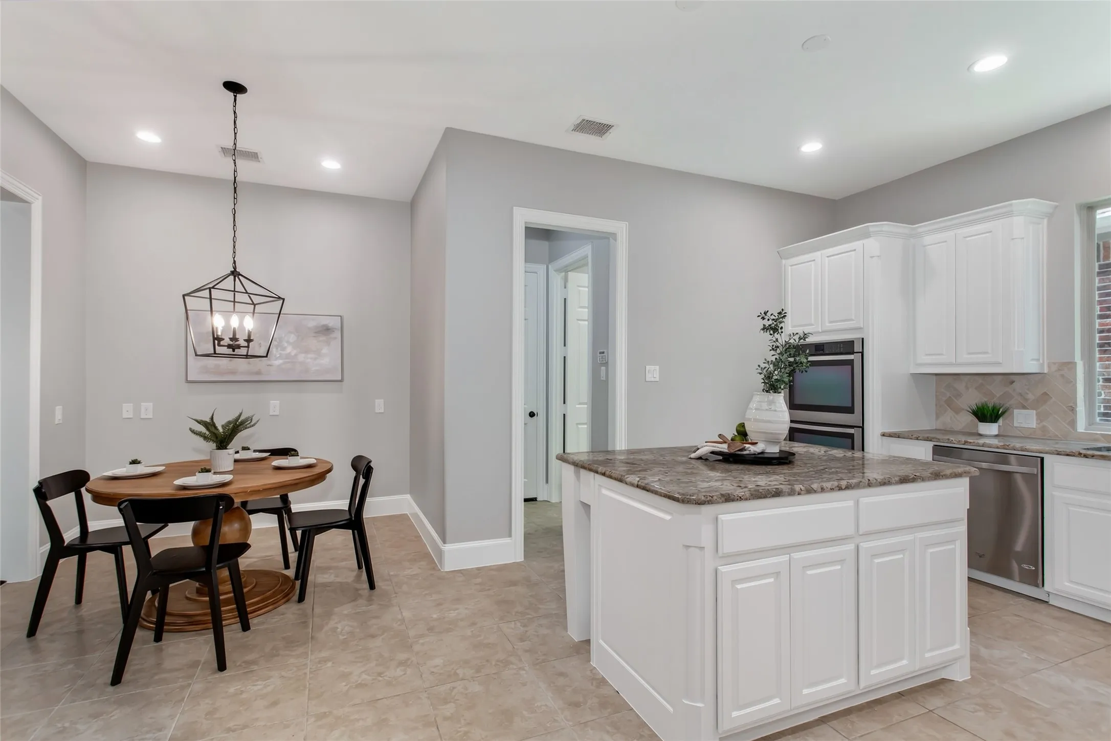 Granite island with cabinet storage sits between the kitchen and a breakfast nook lit by a new 2026
lantern pendant. Tile flooring runs through both spaces, with recessed lighting overhead.