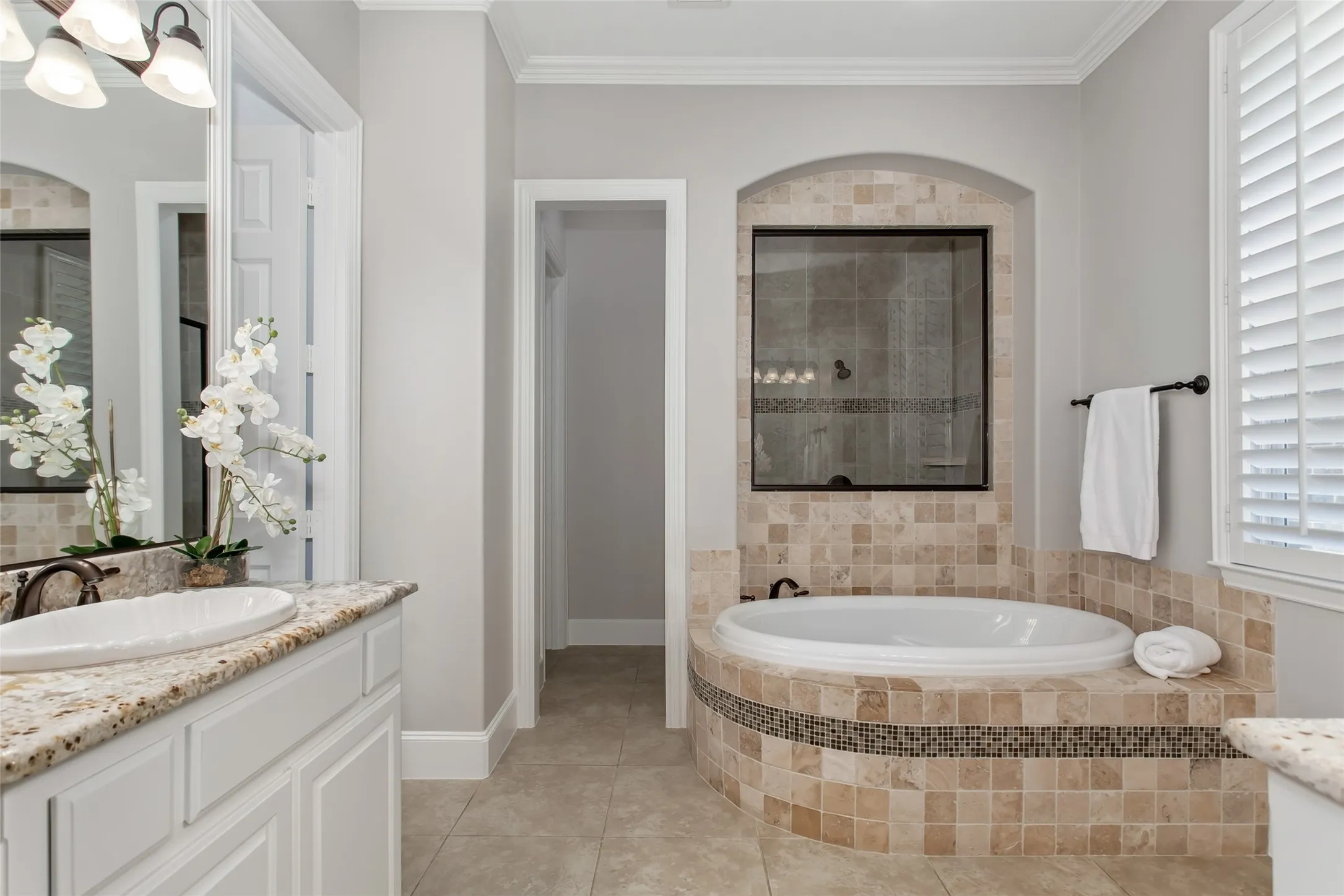 Garden tub with a tumbled travertine surround and glass mosaic accent band set below an arched
niche with a glass window into the shower. Granite vanity, oil-rubbed bronze fixtures, and plantation
shutters.