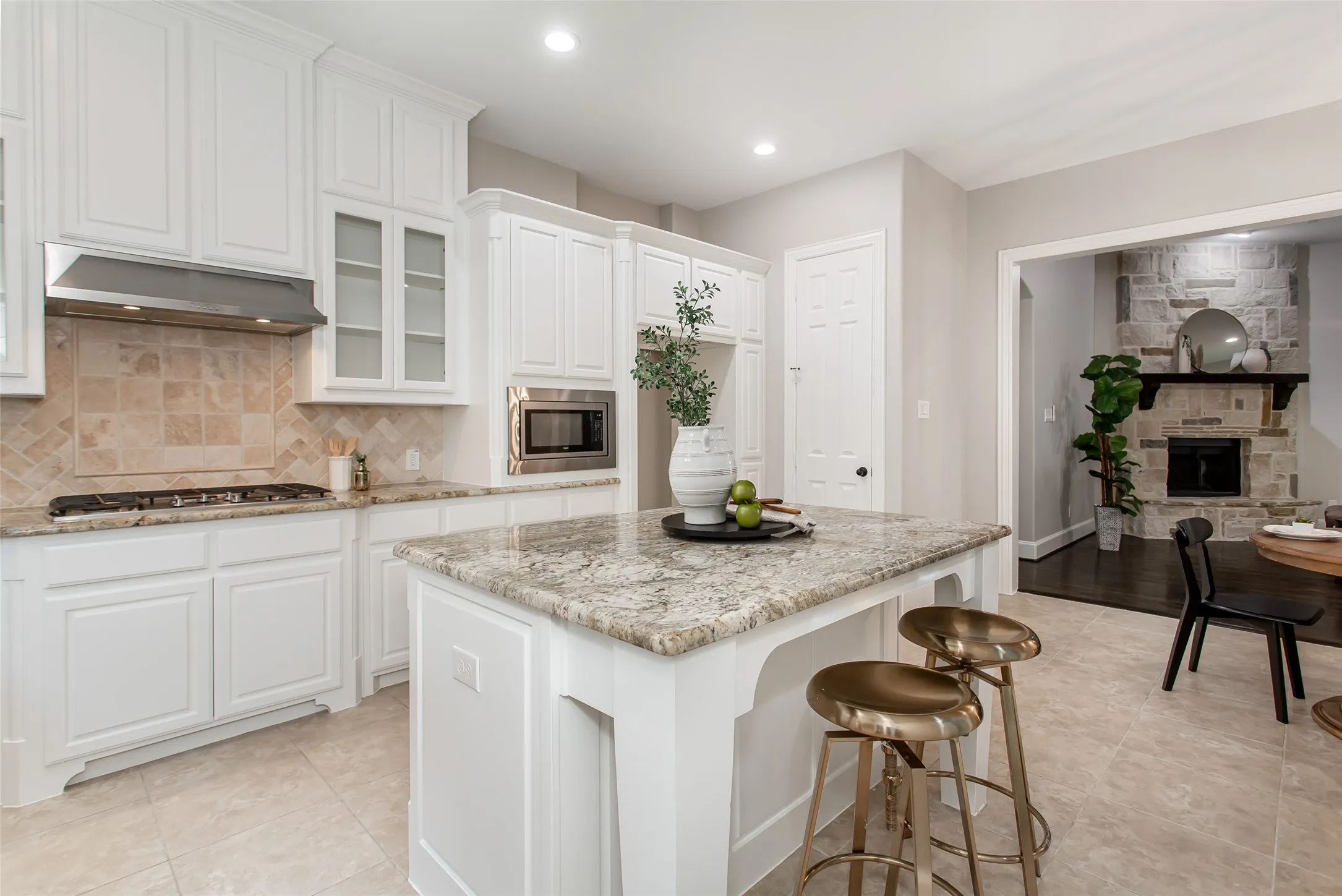 Granite island with bar seating looks across the breakfast area to the stone fireplace in the family room.
Stainless vent hood, built-in microwave, and pantry door on the back wall.
