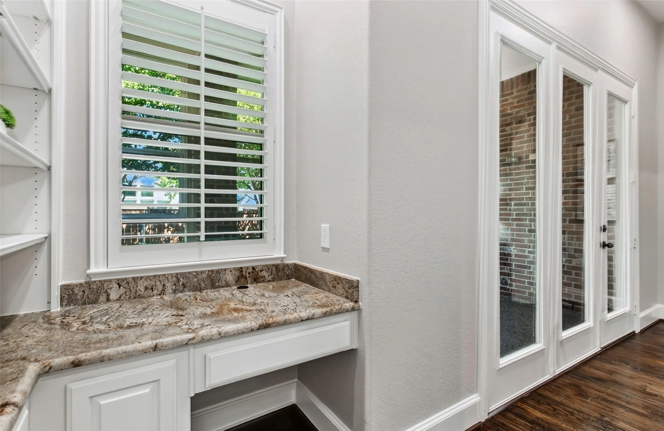 The family room flows to a built-in home management area with open shelving, a granite counter, and
cabinet storage. French doors on the right open to the enclosed sunroom.