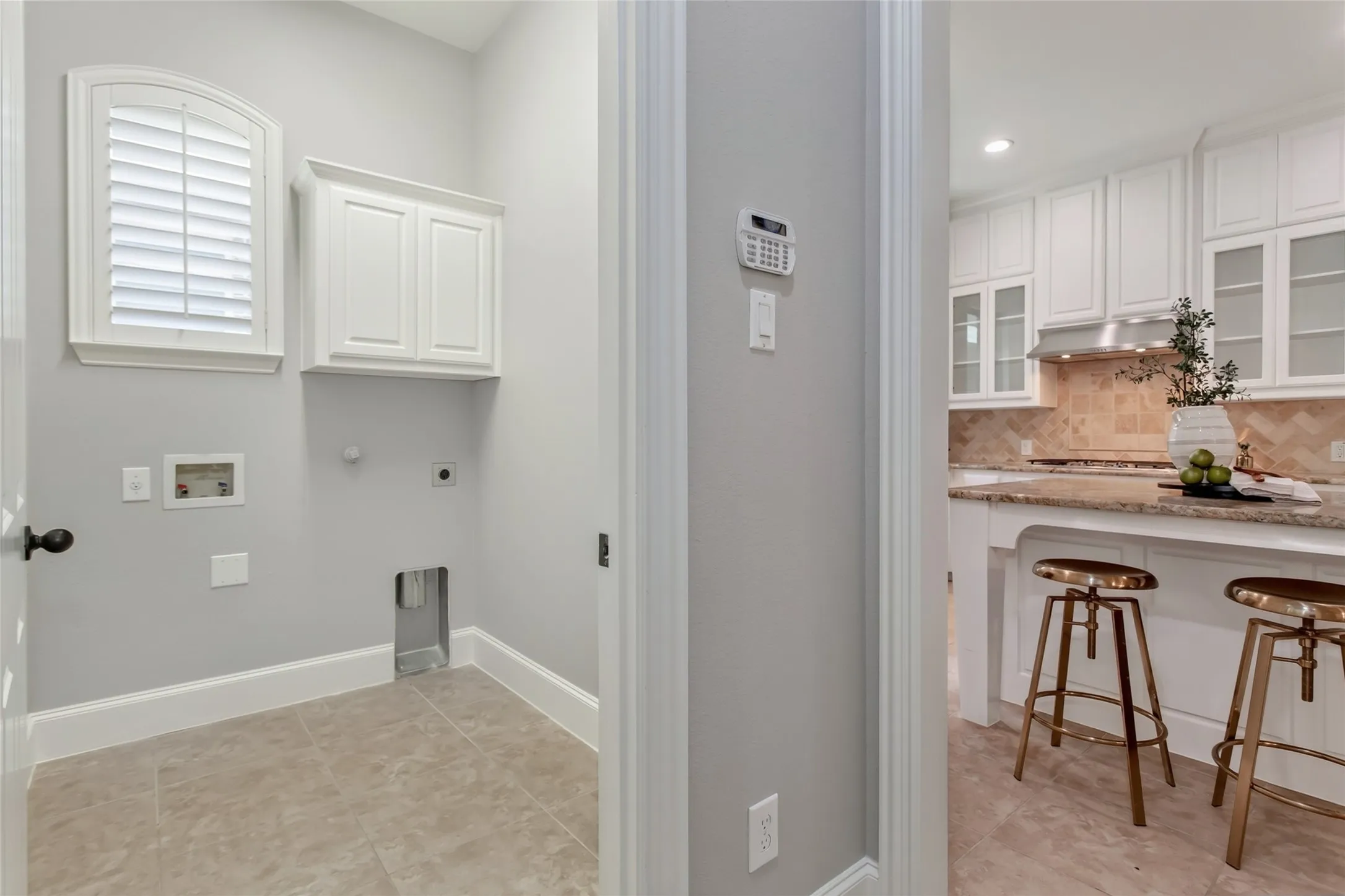 Utility room off the kitchen with tile flooring, an upper storage cabinet, and an arched window with
plantation shutters. Washer and dryer connections on the back wall.