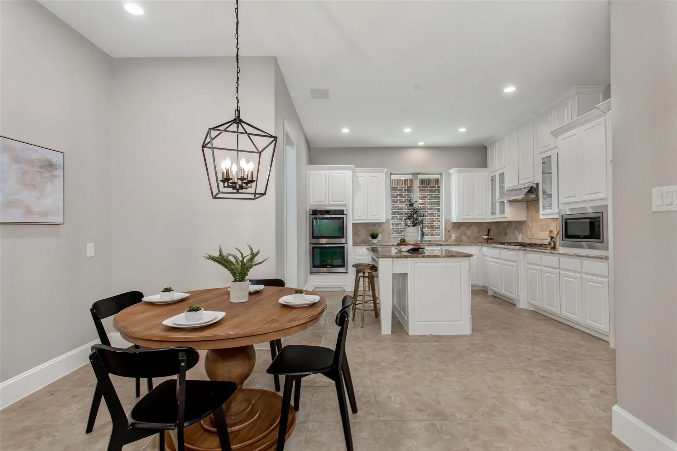 Breakfast nook with tile flooring and a new 2026 lantern pendant opens to the kitchen. Stainless double
wall ovens, a center island, and white cabinetry with crown molding.