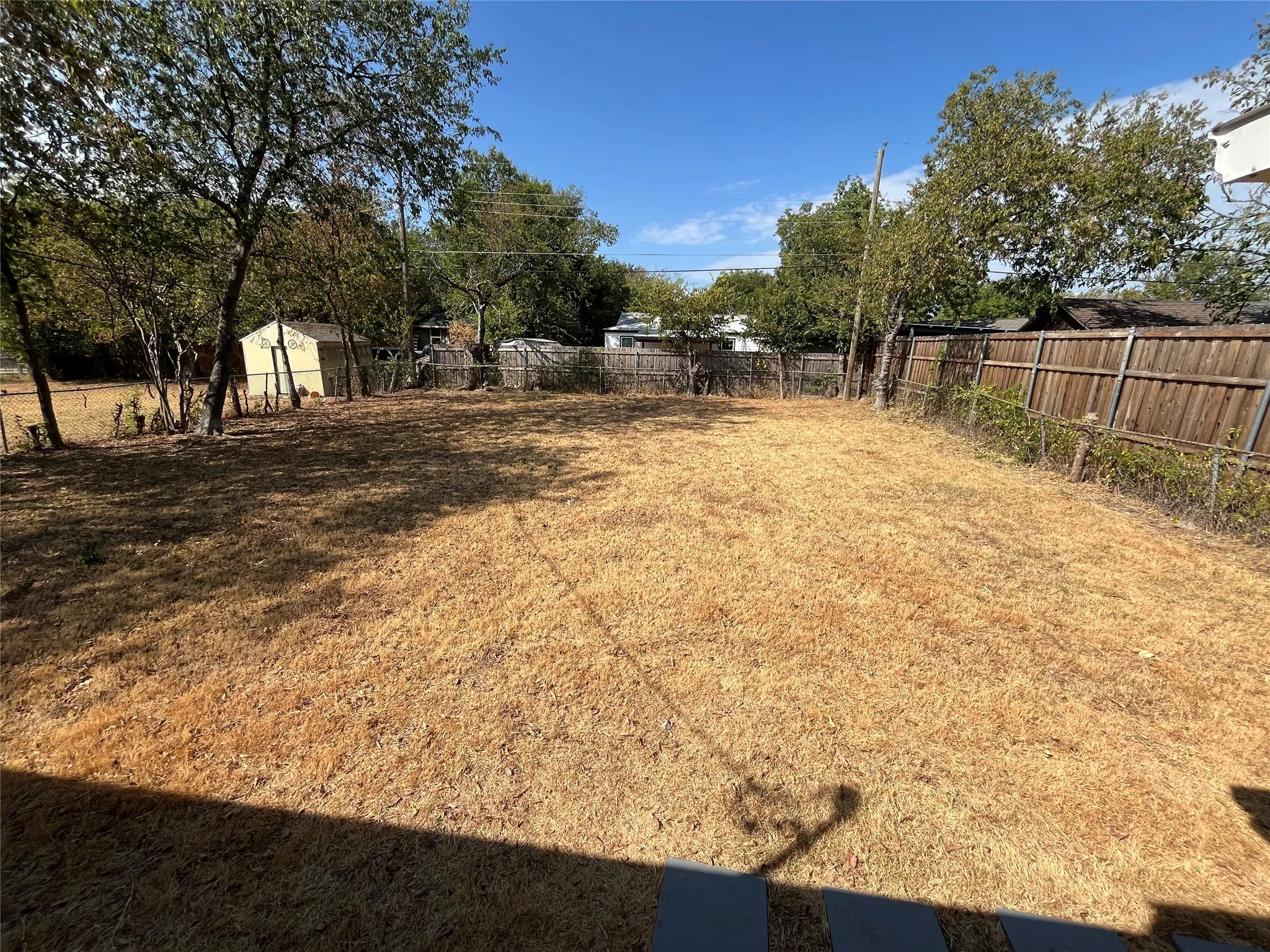 Expansive backyard area with a perimeter wood fence, mature trees, and a visible storage shed