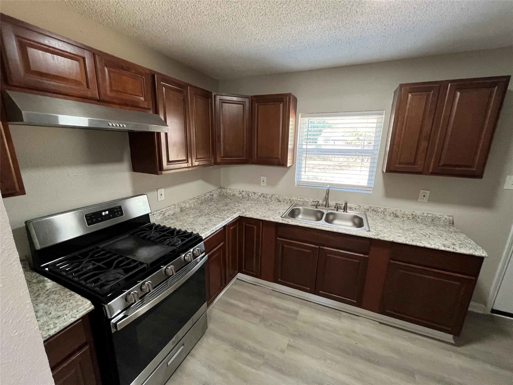 Kitchen featuring wood-finish cabinetry, stainless steel appliances, granite-look countertops, a double basin sink, and wood-look flooring
