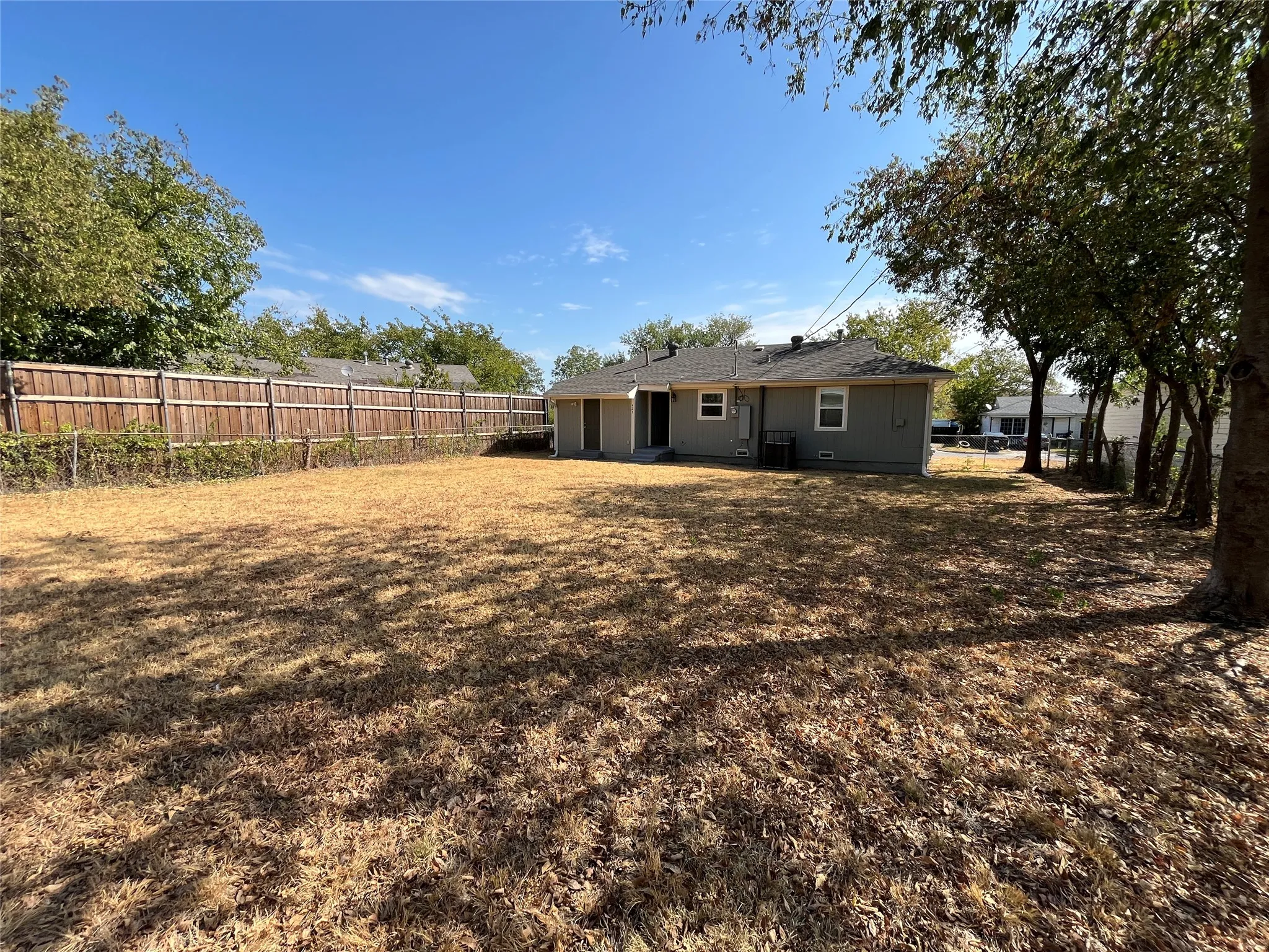 Spacious backyard with privacy fencing, mature trees, and a single-story residence