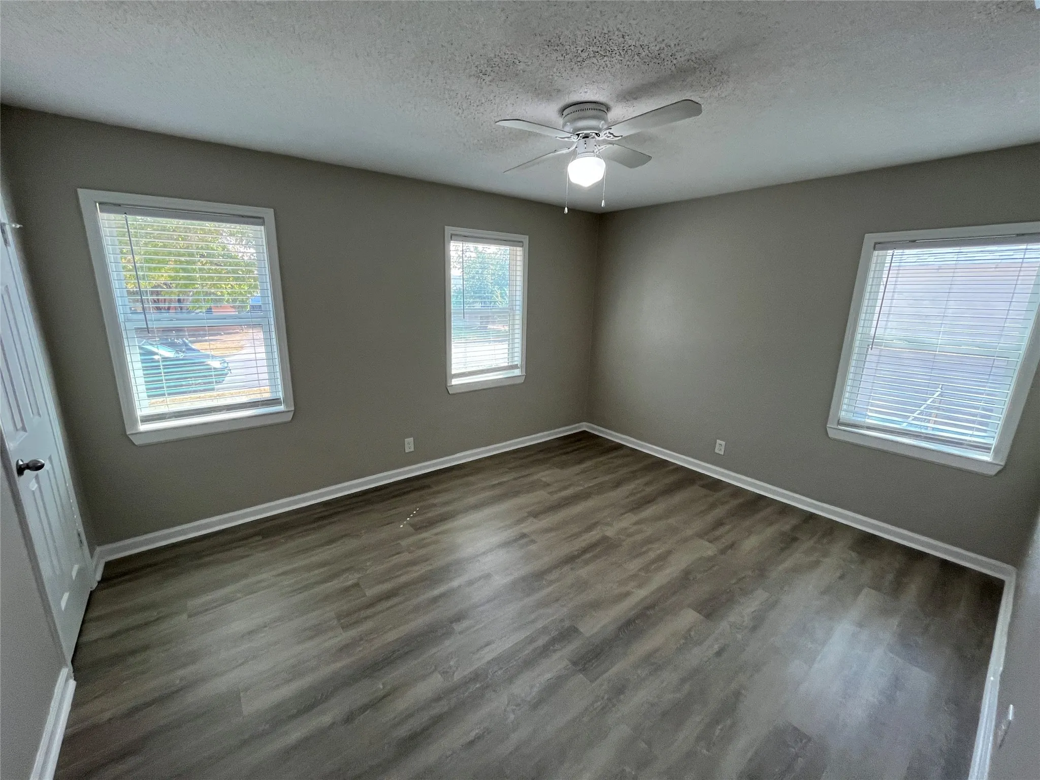 Contemporary ceiling fan with integrated lighting, wood-finish flooring, multiple windows with blinds, and neutral painted walls