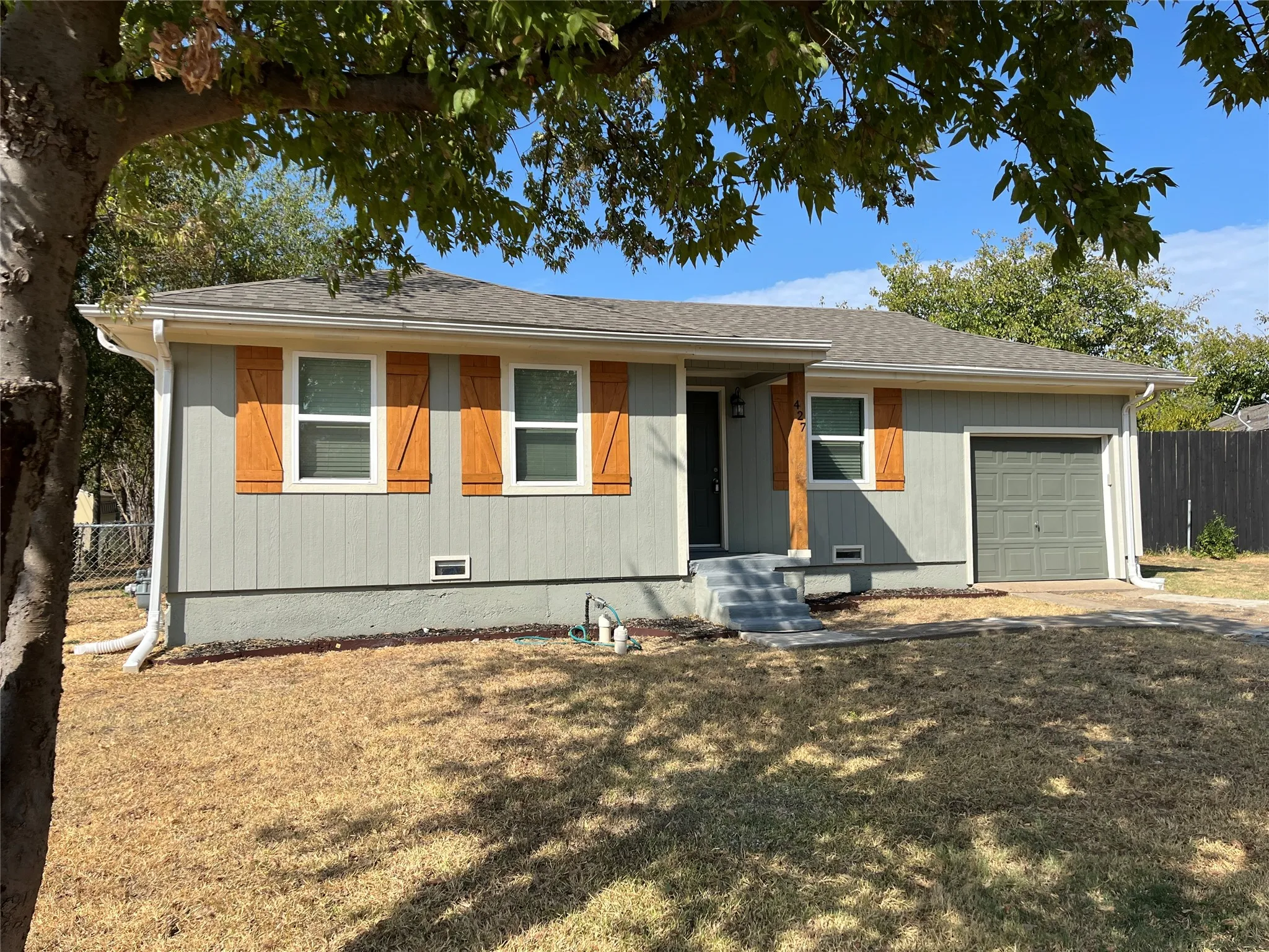 Single-story residence featuring a gray exterior, wood-finish shutters, a covered entry, and an attached garage
