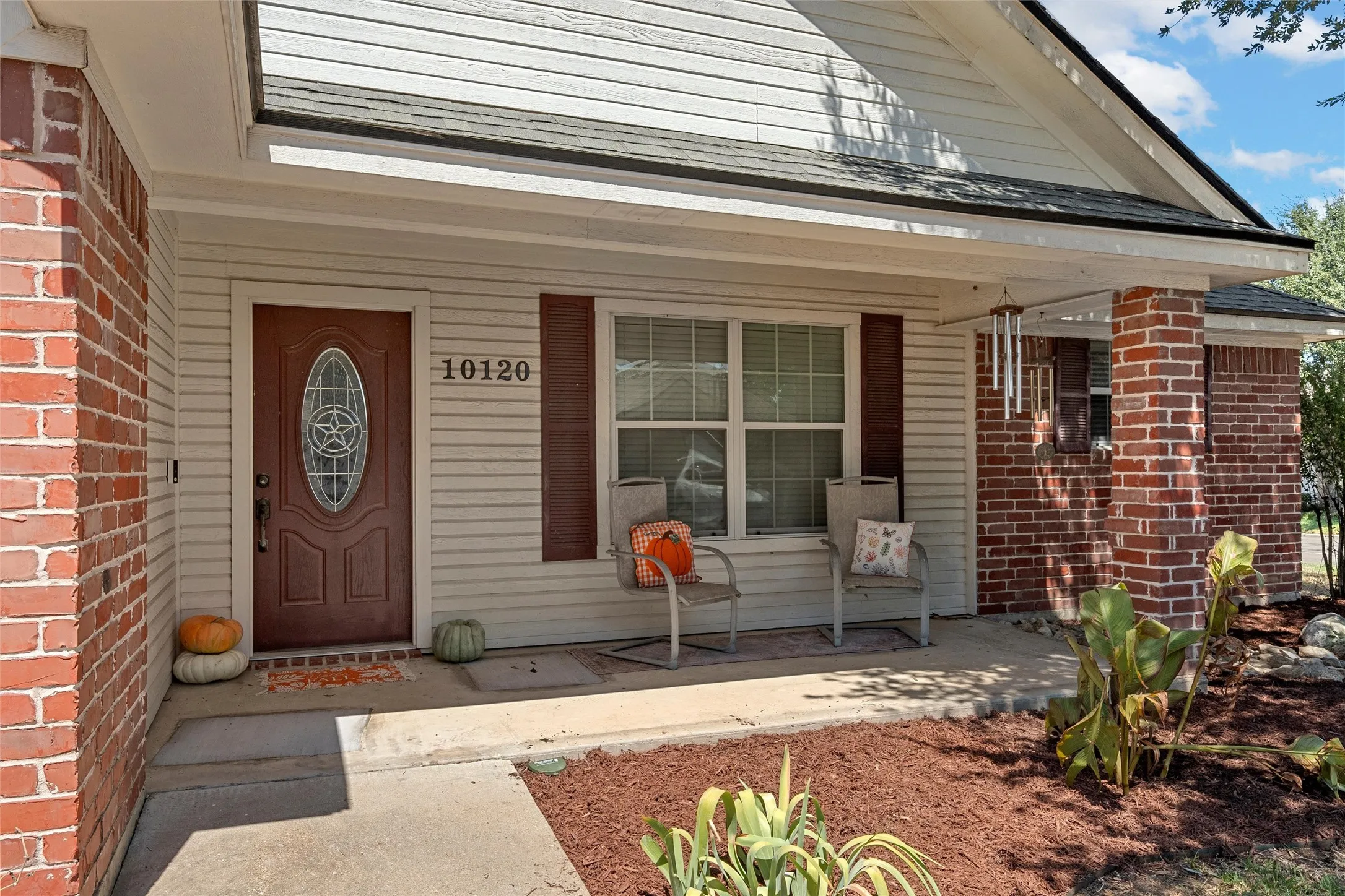 Brick and siding exterior with a covered porch, featuring a substantial entryway and a window with functional shutters
