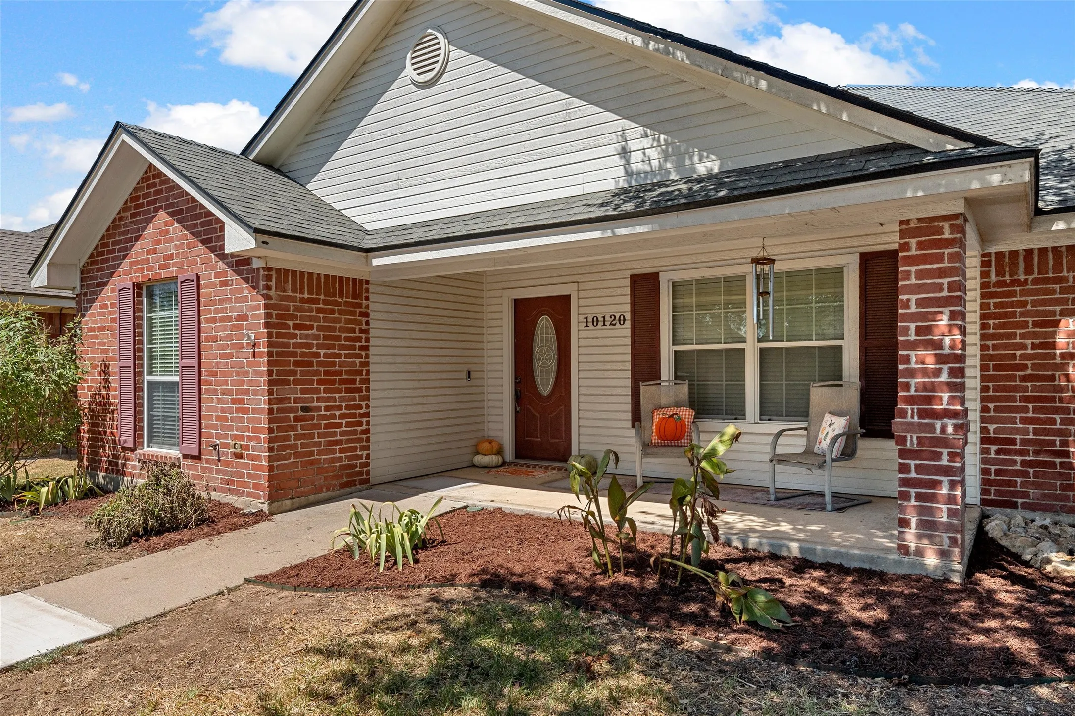 Brick and siding exterior with a covered porch, concrete walkway, and landscaped garden beds