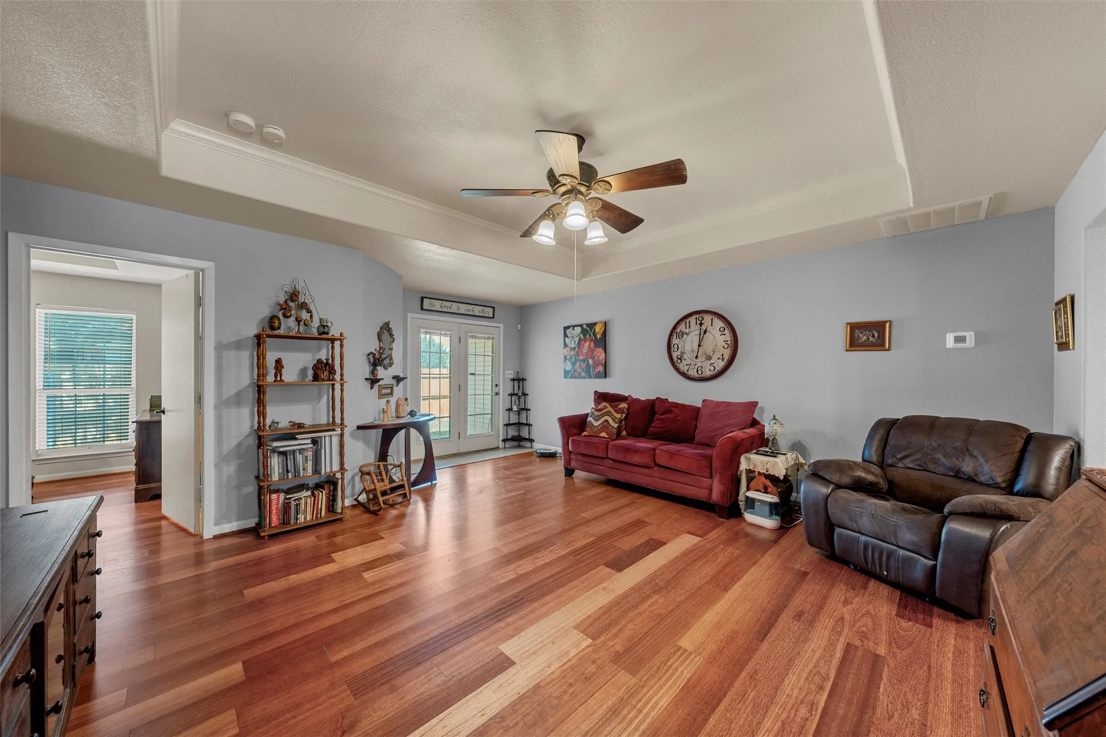 Spacious room featuring wood-finish flooring, a tray ceiling, and a ceiling fan with integrated lighting