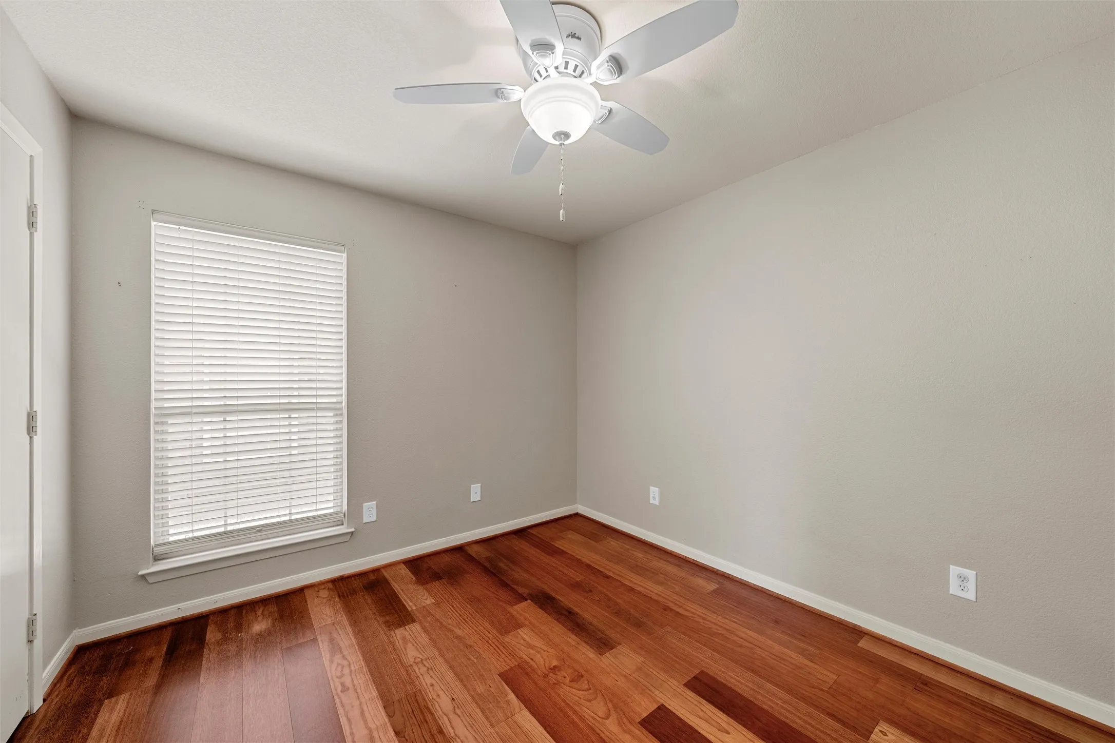 Hardwood flooring, window with blinds, ceiling fan with integrated lighting, neutral wall tones