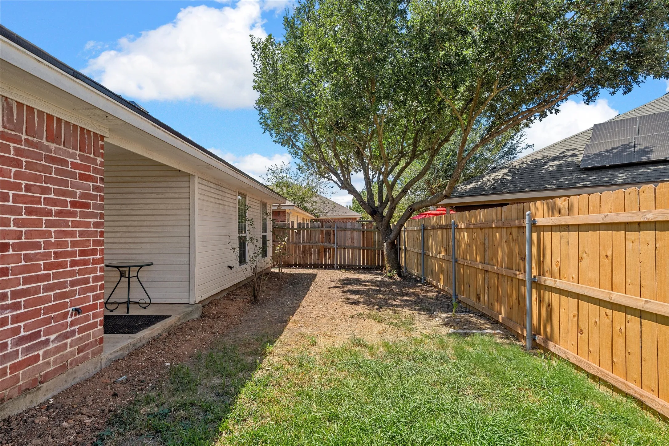 Red brick exterior, covered patio, white siding, wood privacy fence, and mature tree