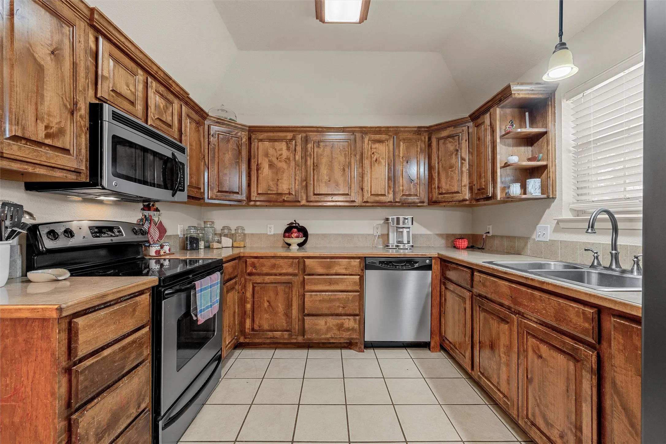Kitchen featuring wood cabinetry, stone-finish countertops, stainless steel appliances, and a tile backsplash