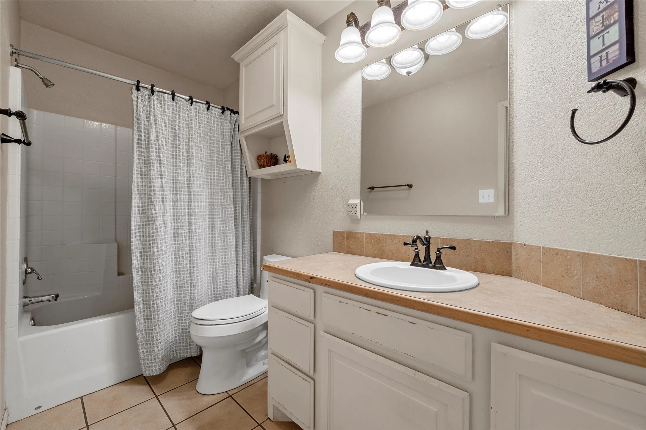 White vanity with an integrated sink, bronze-finish faucet, and a stone-look countertop with a tile backsplash