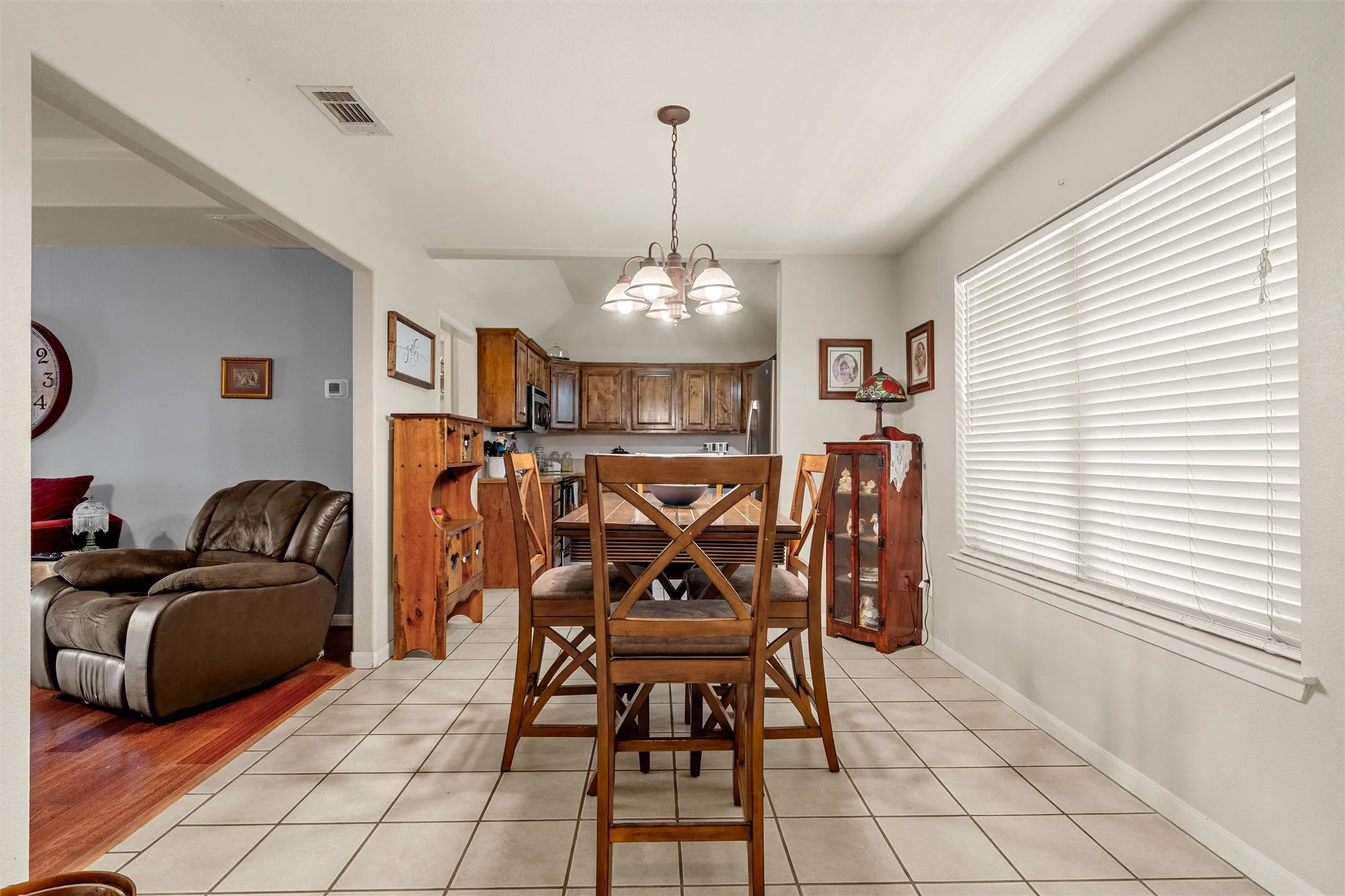 Open-concept dining area featuring tile flooring, a multi-light chandelier, and a large window with blinds