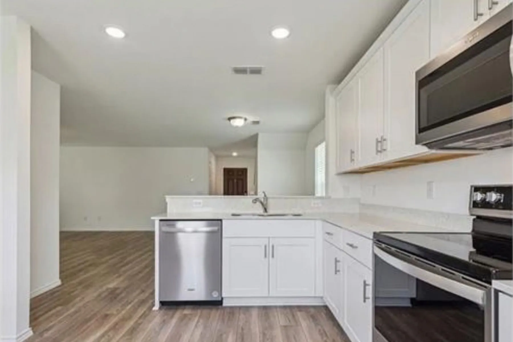 Modern kitchen featuring white cabinetry, light-colored countertops, stainless steel appliances, and wood-finish flooring
