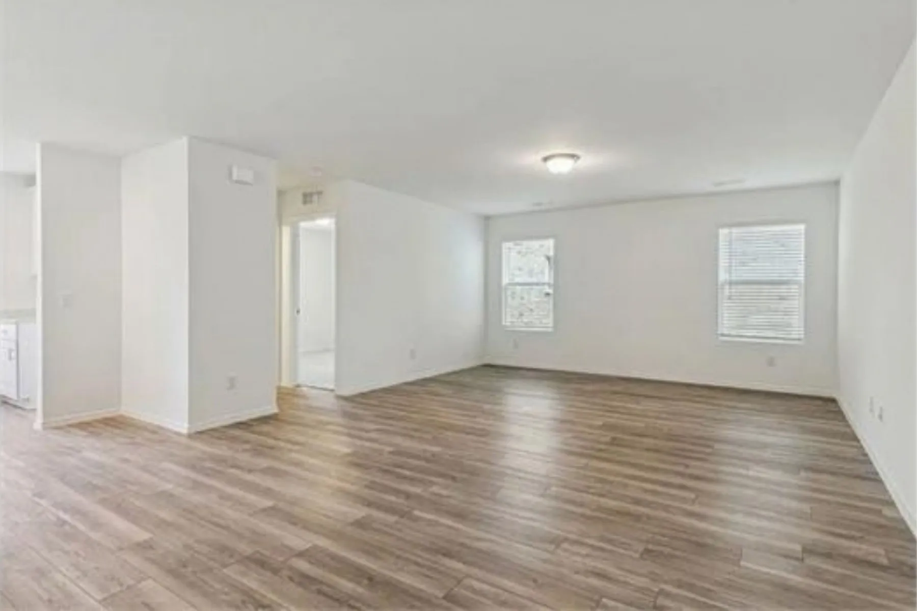 Open-concept living space with wood-finish flooring, white walls, and multiple windows