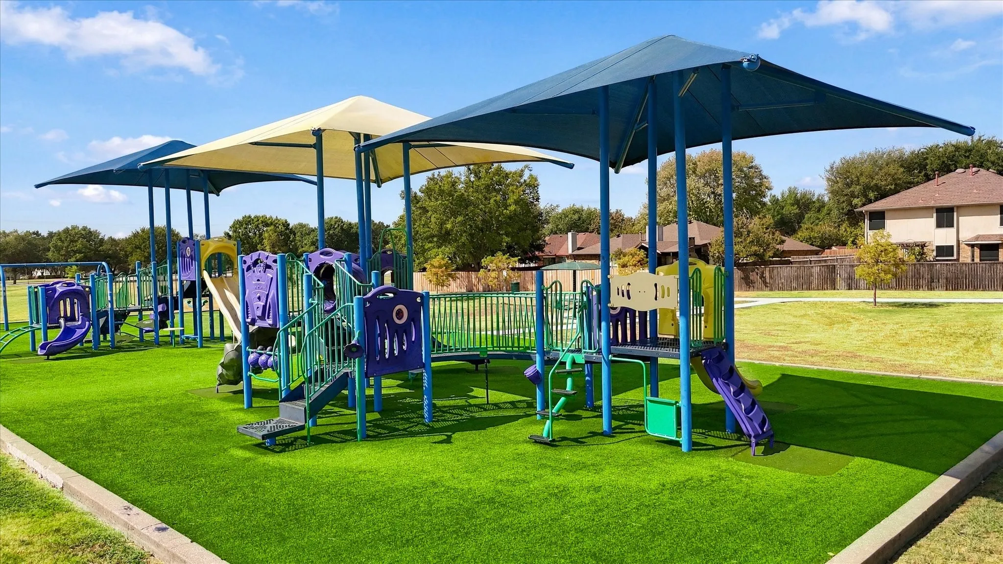 Playground with shade canopies, multiple slides, and climbing structures on artificial turf