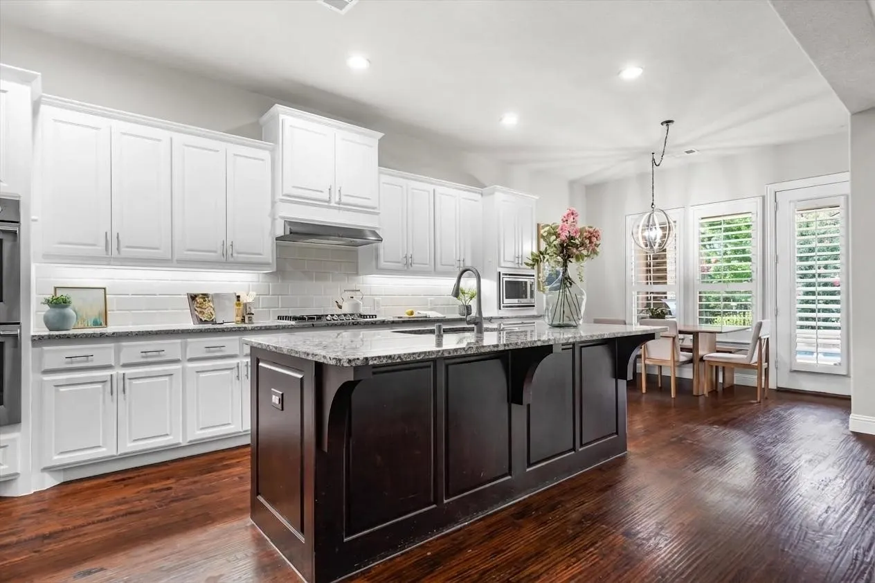 A generous granite-topped island offers prep space and seating, surrounded by abundant white cabinetry and hardwood floors.
