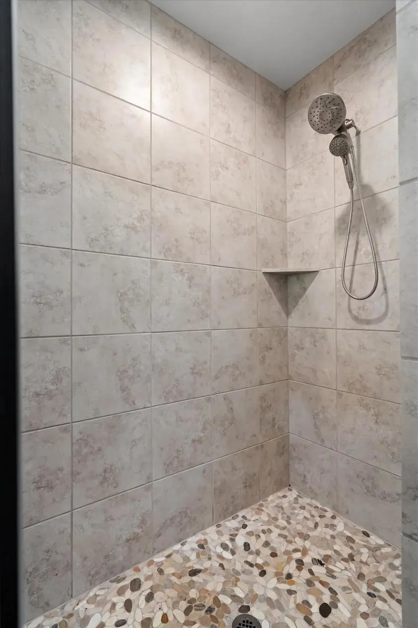 Custom tile walk-in shower with pebble-stone floor detail and built-in corner shelving.