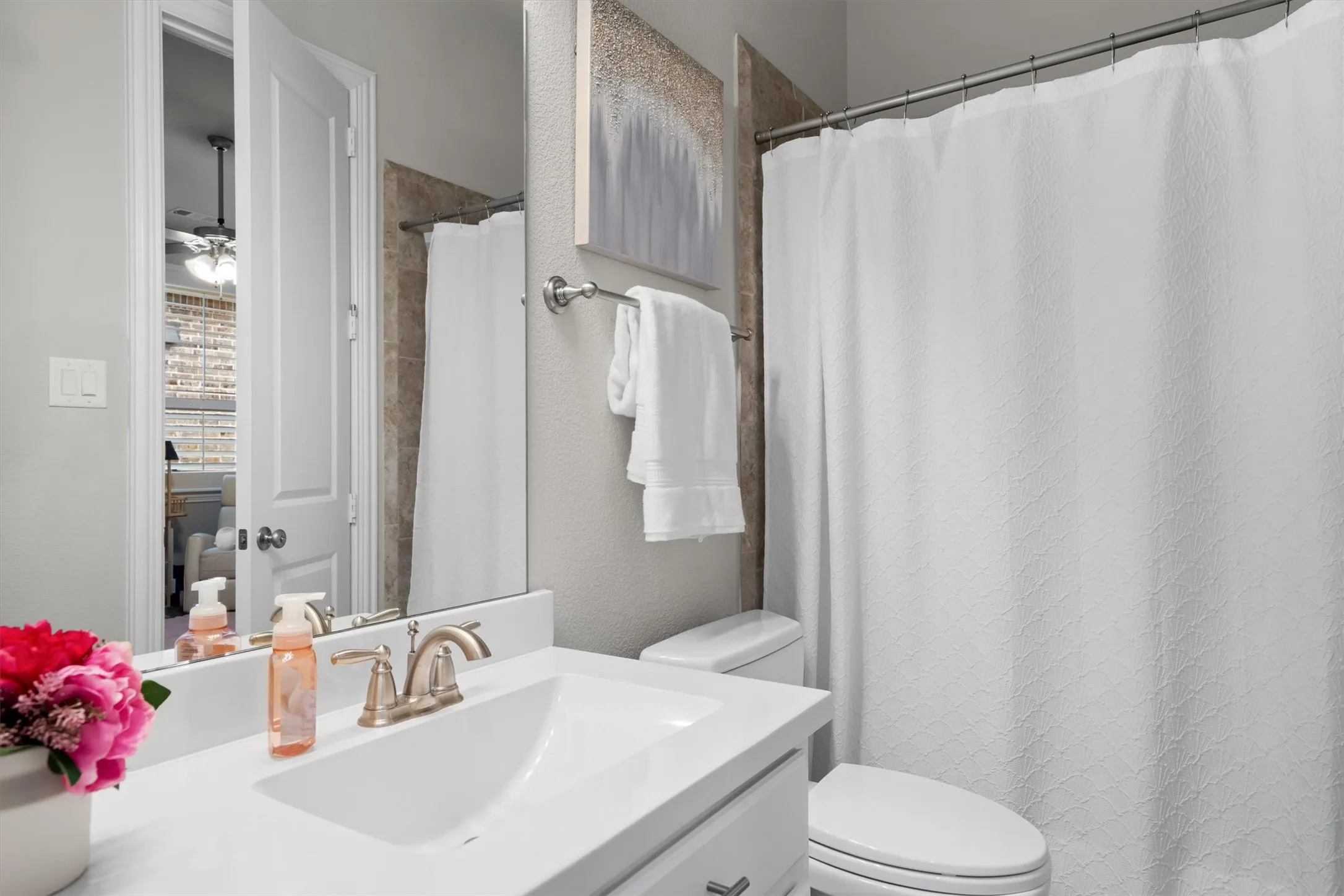 A full bathroom with quartz-topped vanity, brushed gold fixtures, and tub/shower combo.