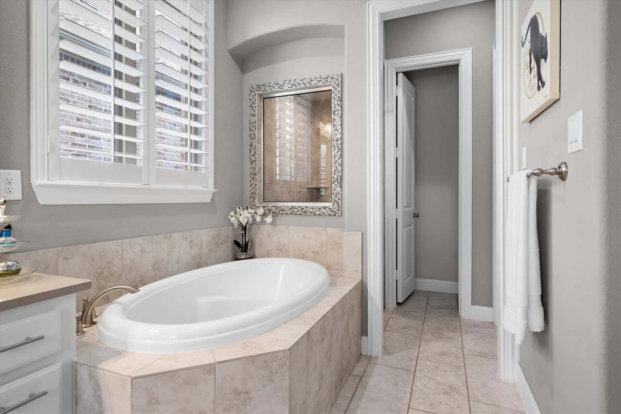 A garden soaking tub set beneath plantation-shuttered windows with custom tile surround and mirrored accents.