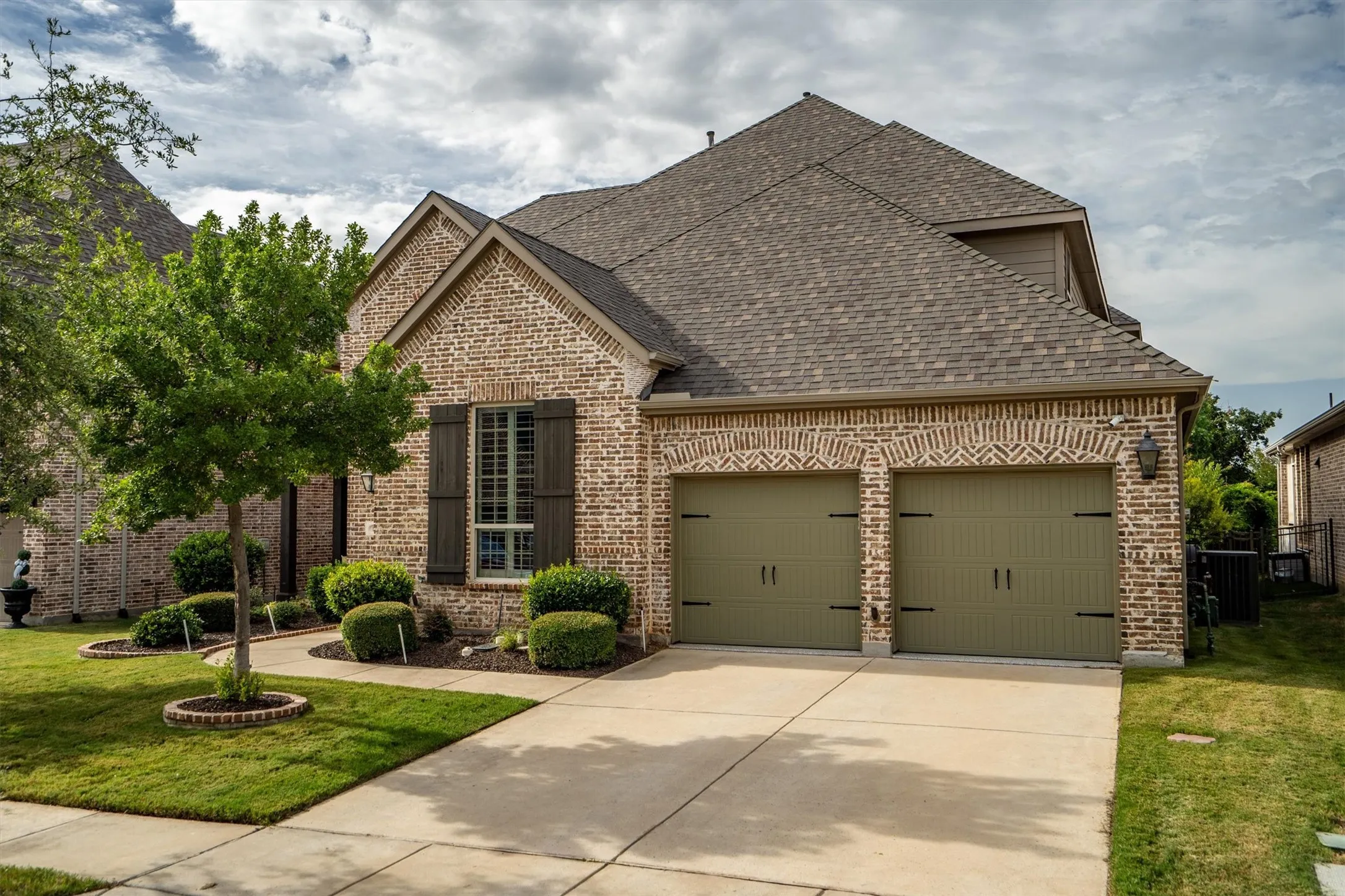Classic brick exterior with designer carriage-style garage doors, professional landscaping, and a wide driveway approach.