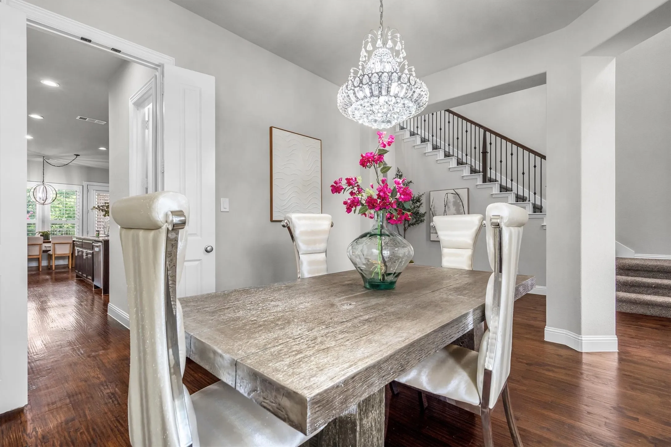 A statement chandelier crowns this light-filled dining space with hardwood floors and open sightlines to the staircase beyond.