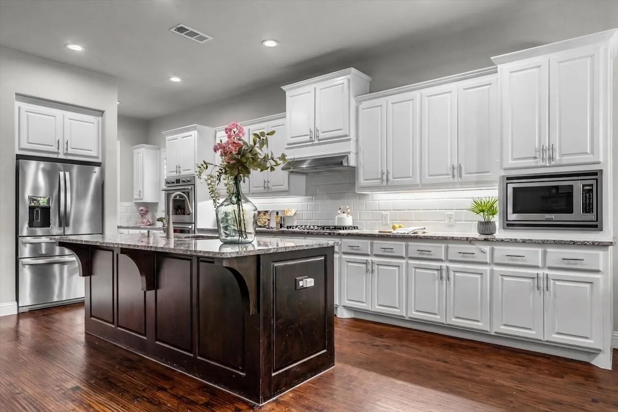 Crisp white cabinetry, stainless appliances, and a contrasting dark wood island with granite countertops define this stylish kitchen.