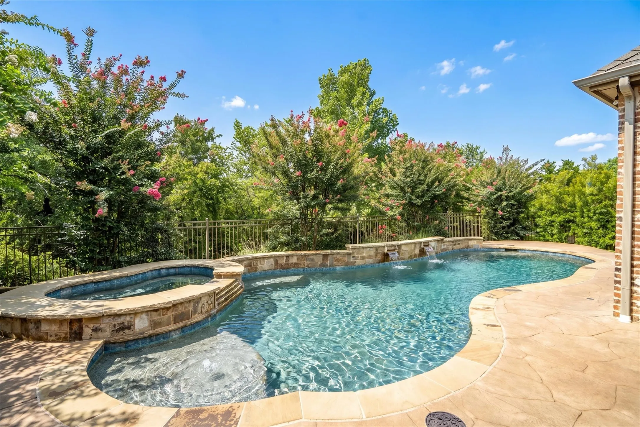 Another stunning angle of the free-form pool, raised spa, and travertine-style decking framed by crepe myrtles.