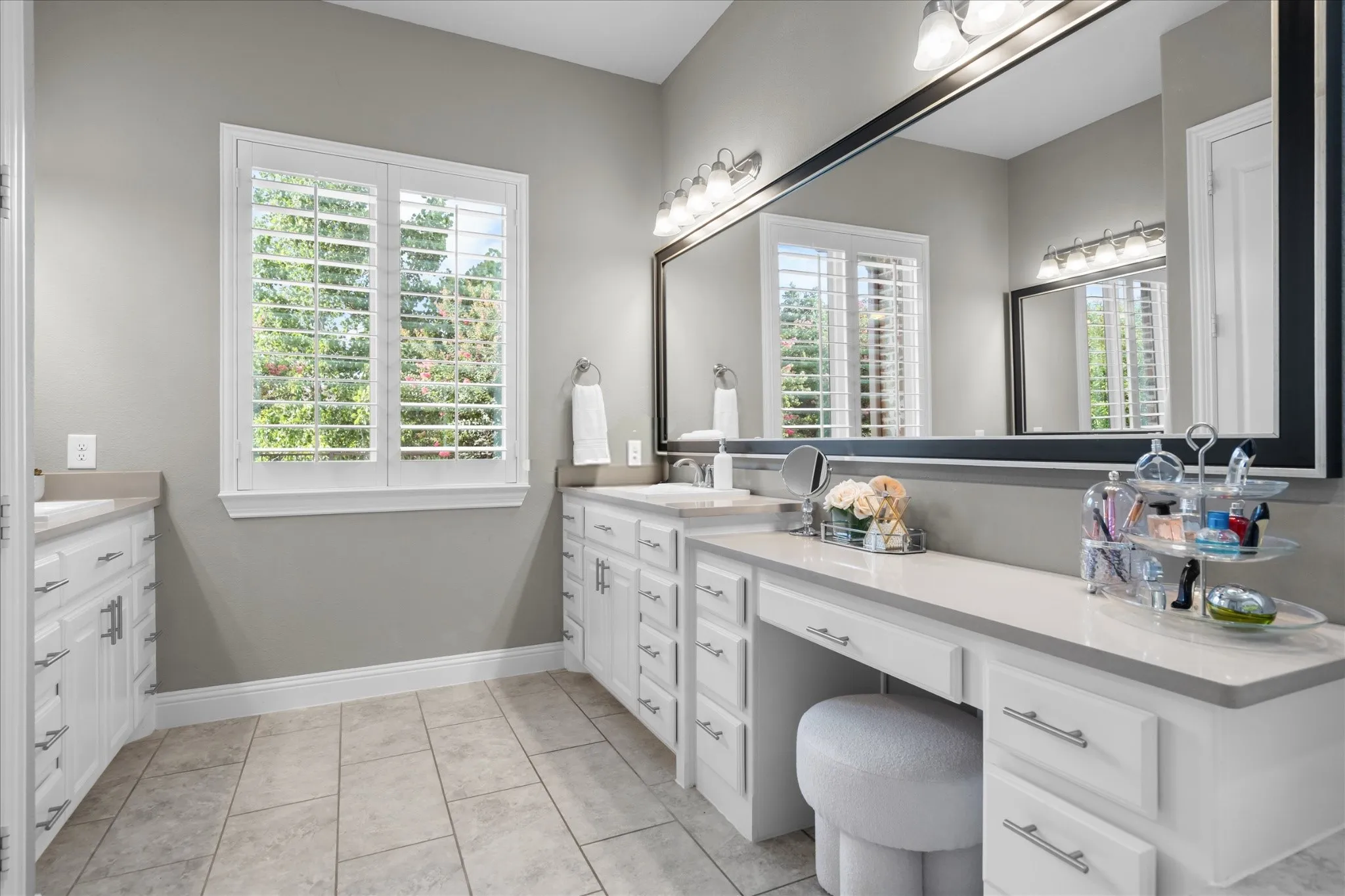 An extended dual-vanity configuration with seated makeup station, framed mirrors, and plantation shutters.