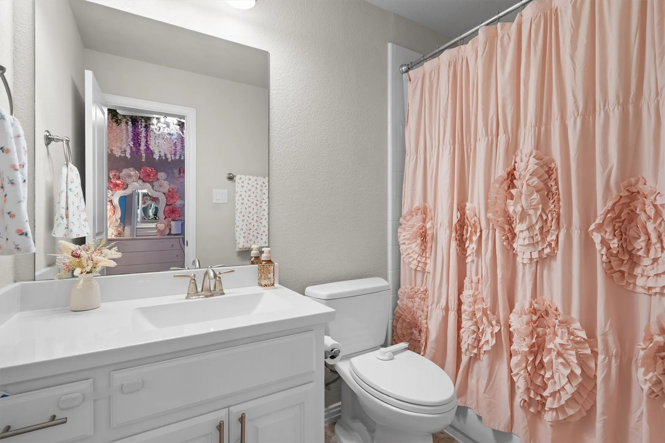 A full bathroom with white vanity, ruffled designer curtain, and tub/shower combo.