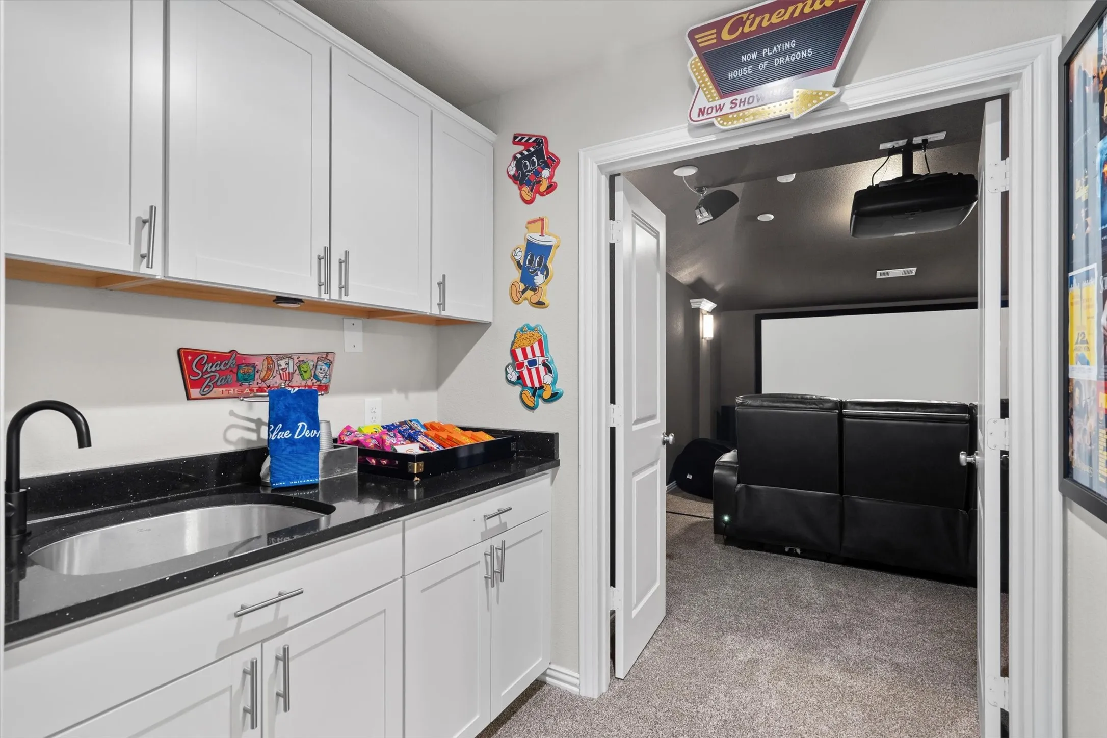 A convenient wet bar with sink, black granite counters, and white cabinetry opens to the media room.
