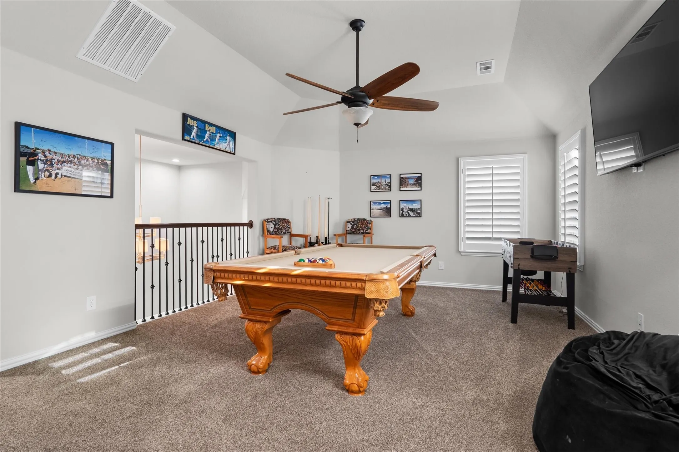  A spacious carpeted game room with vaulted ceiling, ceiling fan, and room for a pool table and more.