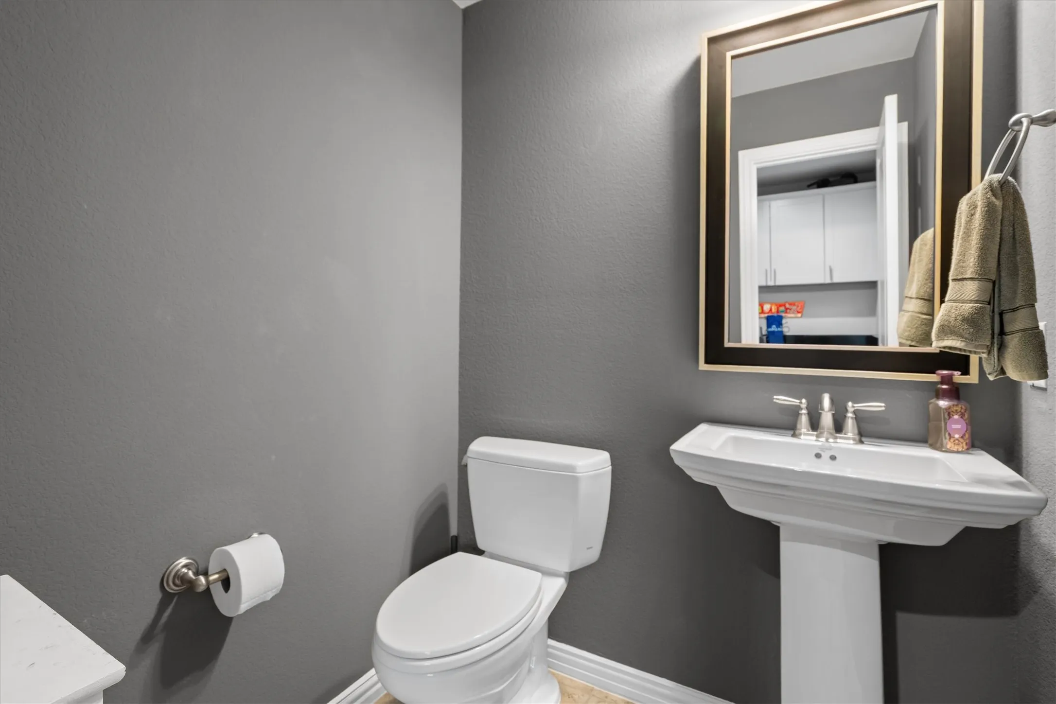 A chic powder bath with pedestal sink, framed mirror, and designer gray walls.