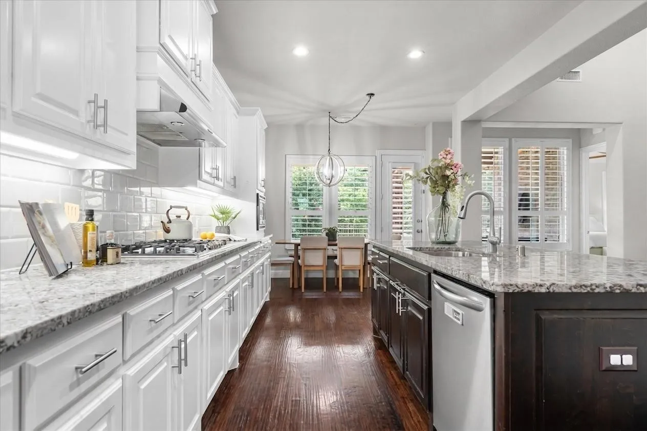 Granite countertops, a gas cooktop, subway tile backsplash, and stainless dishwasher line this efficient, light-filled workspace.